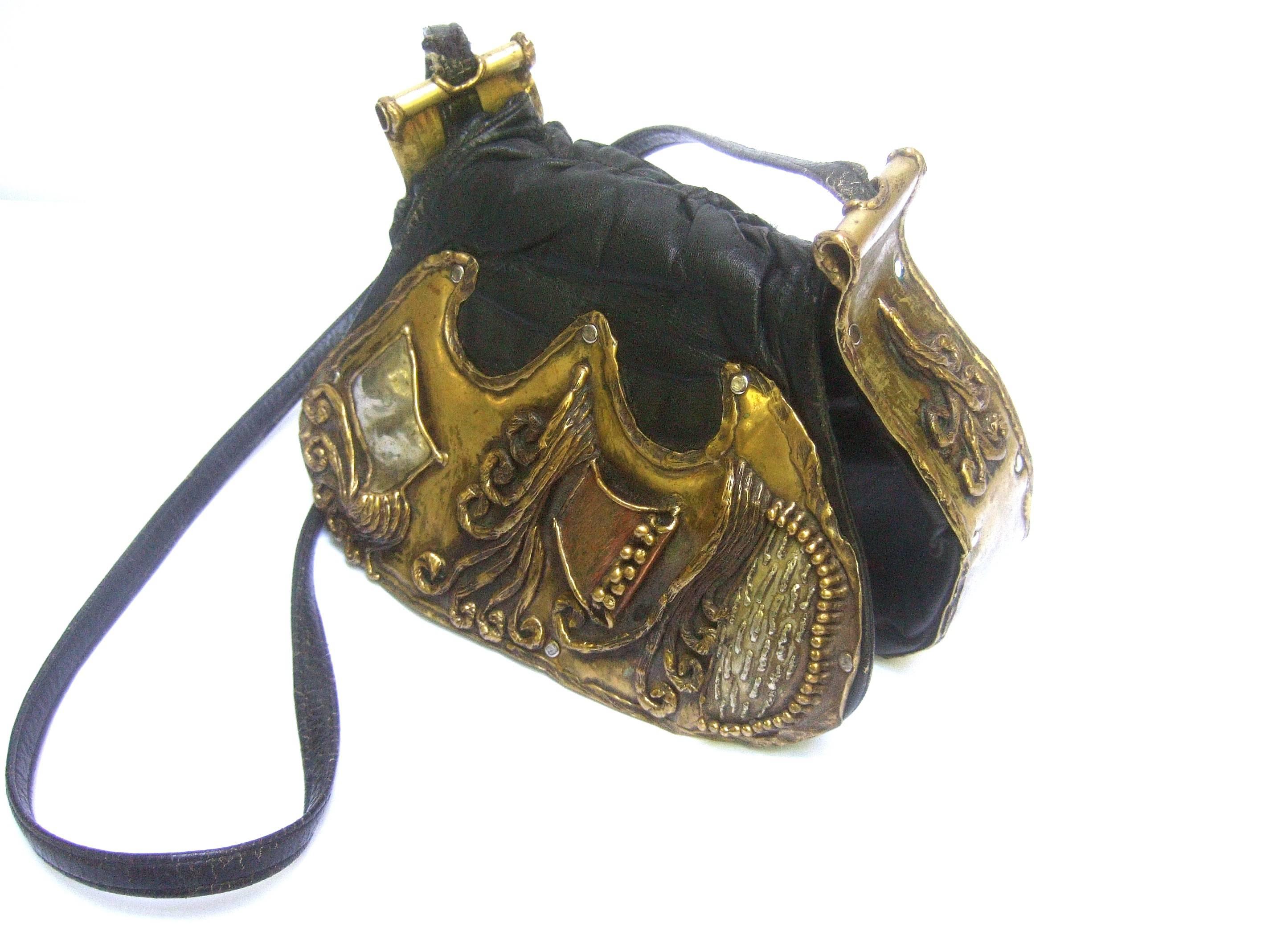 Avant garde brutalist mixed metal artisan handbag ca 1970s
The unique handmade shoulder bag is adorned 
with sinuous three dimensional mixed metal work
designs on the black leather flap cover 

The mixed metal work designs are primarily brass
