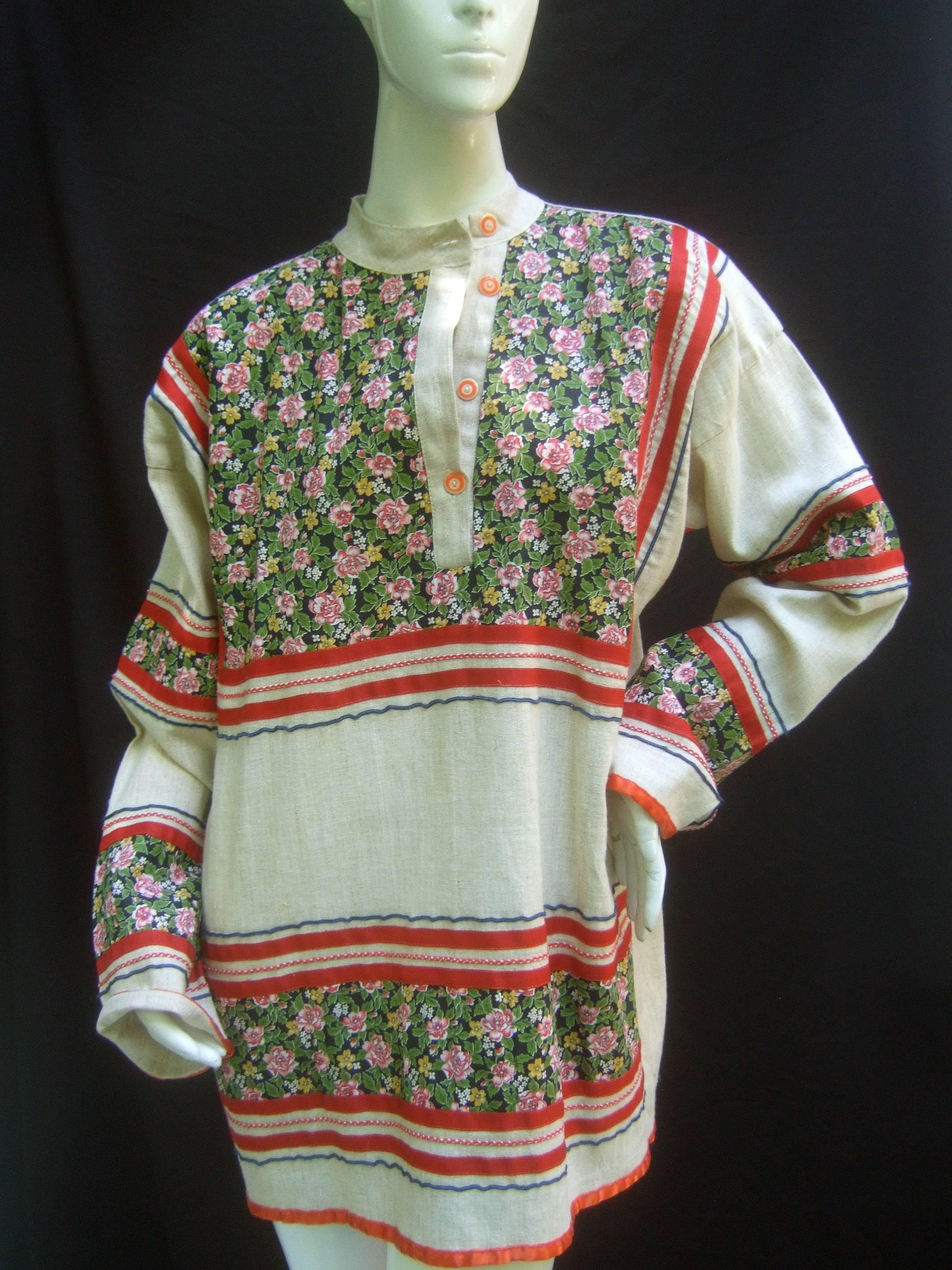 Saks Fifth Avenue Bohemian cotton festival tunic c 1970s 
The hippie chic cotton tunic is designed with floral 
panels that run across the bodice, sleeves and lower
front section

The Nehru style collar buttons with a set of red
and white resin