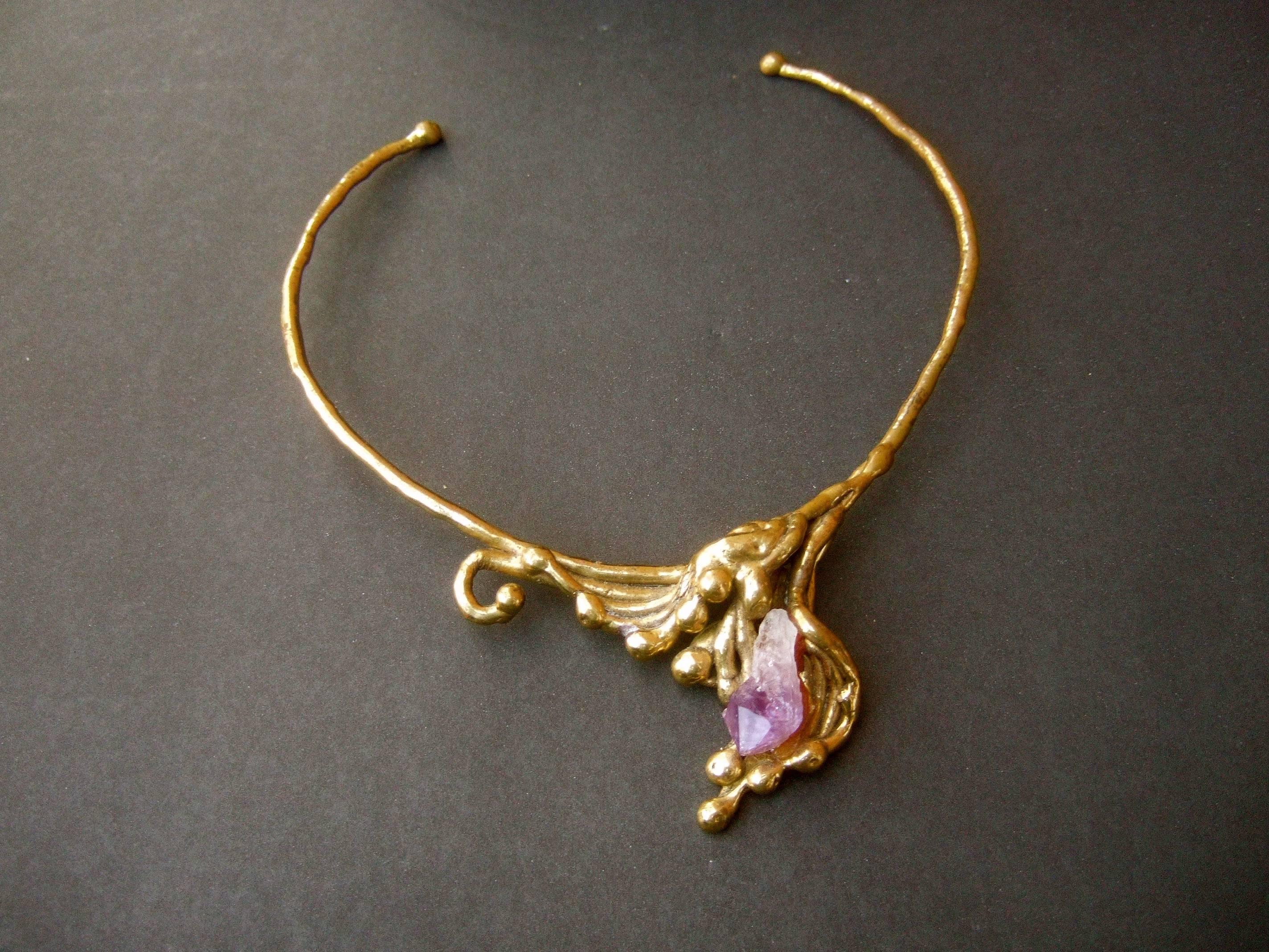 Amethyst brass metal artisan choker necklace c 1970s
The unique handmade choker necklace is designed 
with a rigid brass metal curved band

The center is embellished with a jagged amethyst stone 
encased in sinuous brass metal bands 

Makes a very