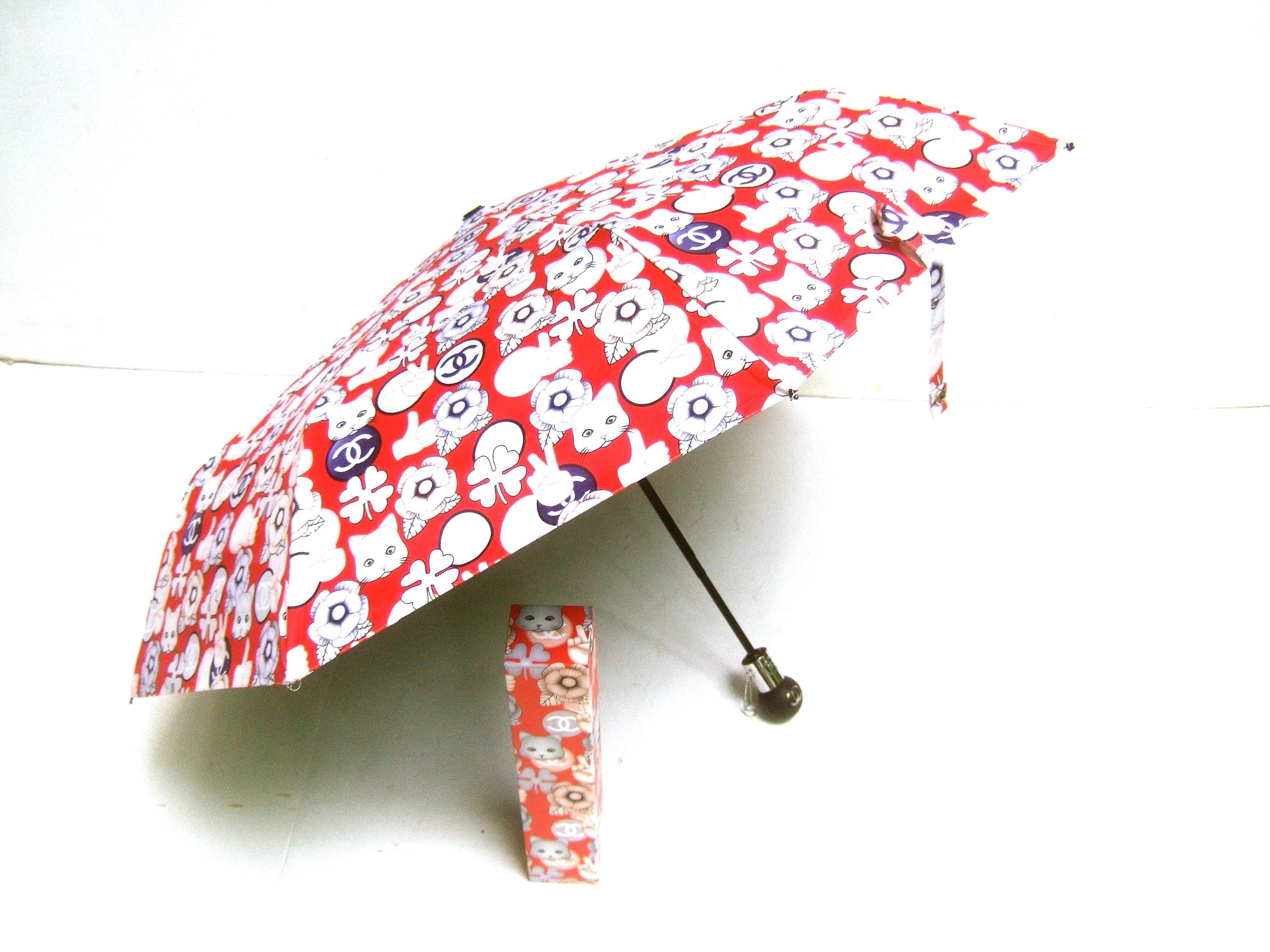 Chanel Whimsical cat theme umbrella in Chanel box 
The stylish red nylon Chanel umbrella is designed with 
cat faces, four-leaf clovers, camellia flowers, hand symbols
and circular logos with Chanel's C.C. initials 

The black resin orb handle is