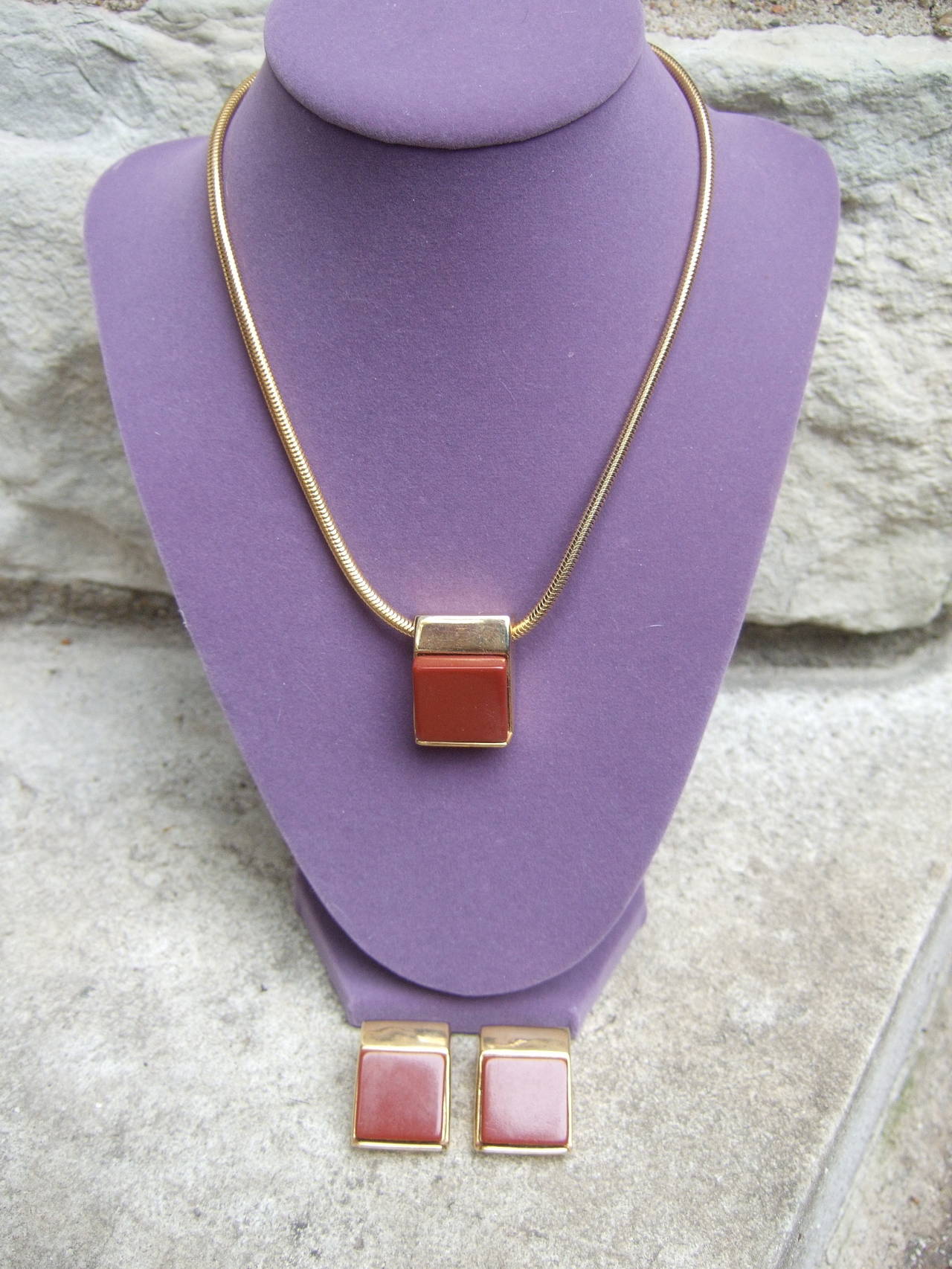 Pierre Cardin Sleek cinnabar resin necklace & earrings c 1970
The minimal design is embellished with a resin cinnabar color
cube pendant at the center of the necklace that hangs from a 
gilt metal snake chain

The clip on earrings echo the