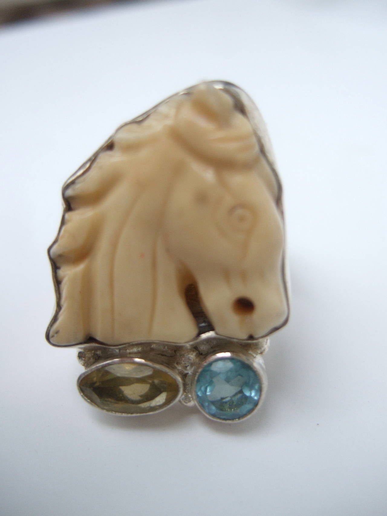 Artisan carved bone horse head sterling ring Size 9 1/2
The handmade sterling ring is adorned with a carved
bone horse head embellished with an aquamarine &
golden citrine faceted semi precious stones

The intricately carved horse head is set