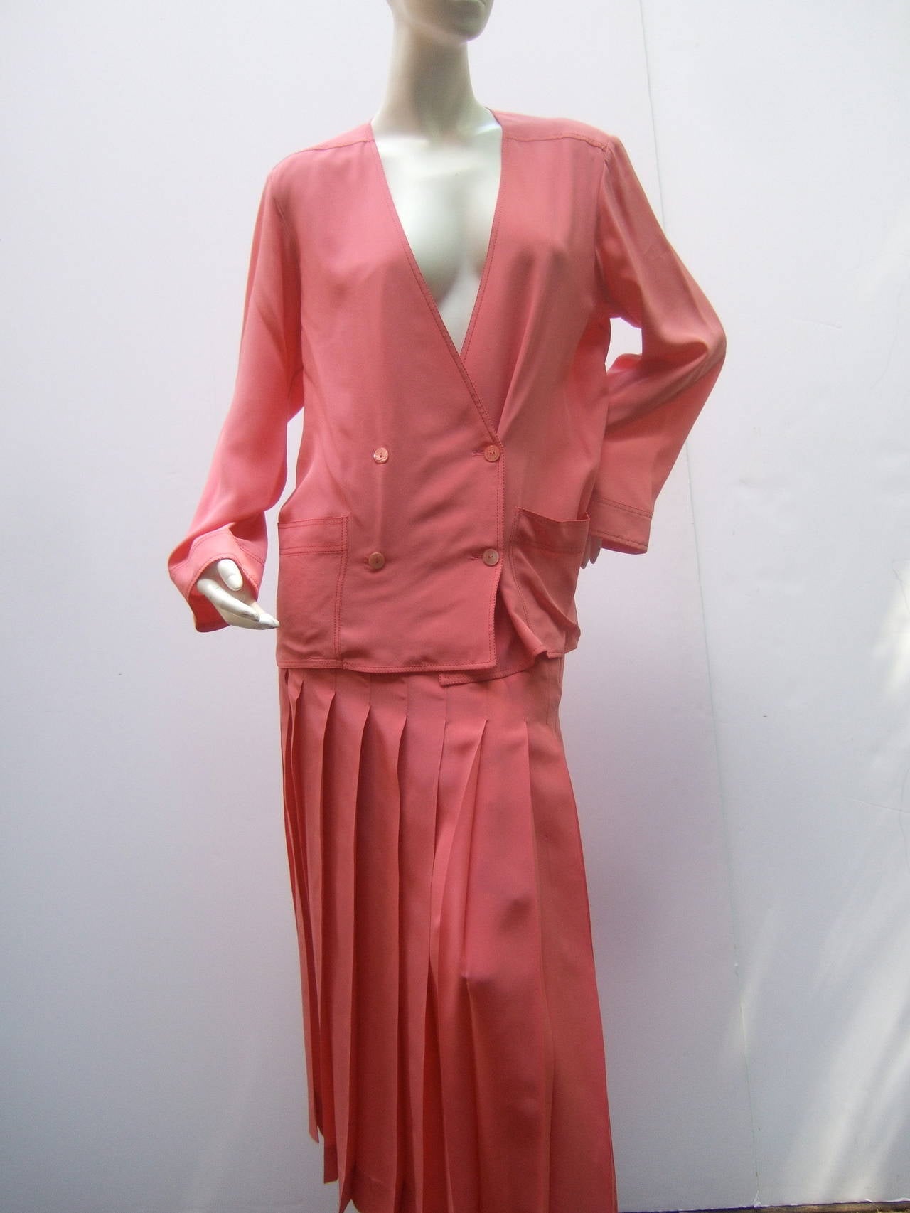 Chanel Vintage silk salmon pink skirt suit c 1980
The elegant skirt suit is designed with luxurious silk
The stylish boxy double breasted jacket has a deep v-neck
design with four Chanel mother of pearl shell C.C buttons
The lower front of the