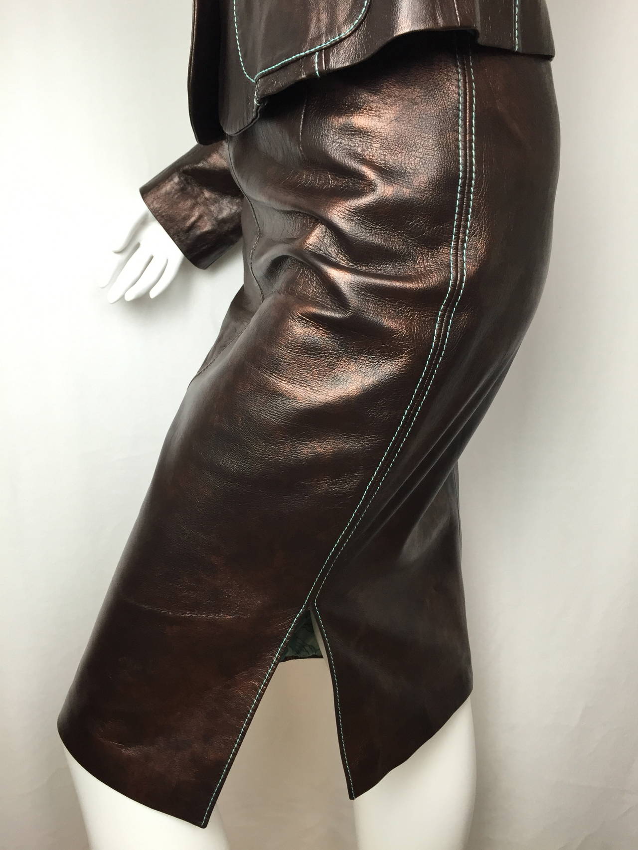Sleek brown leather skirt suit by Christian Lacroix.  Sharp styling.  Made of butter soft brown leather with a coppery iridescent finish that is perfect for day into evening wear.  

70's style aqua top stitching on the jacket and skirt is echoed
