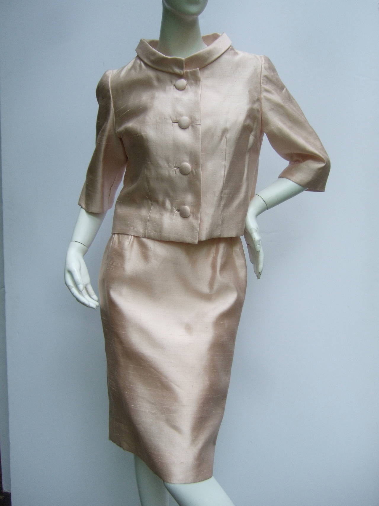 1960s Shantung pale pink jacket & dress ensemble
The chic retro suit is designed with a cropped jacket 
with matching silk buttons. The sleeveless sheath
dress has a sheer lace overlay bodice with glass beading
& clusters of pale pink resin