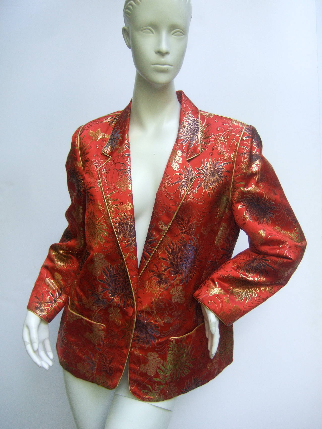 Exotic scarlet chinoiserie brocade jacket c 1980s
The luxurious vintage jacket is designed with luminous
floral brocade fabric with gold metallic piping trim that
frames the lapels, cuffs & pockets

The field of lush flower blooms are set