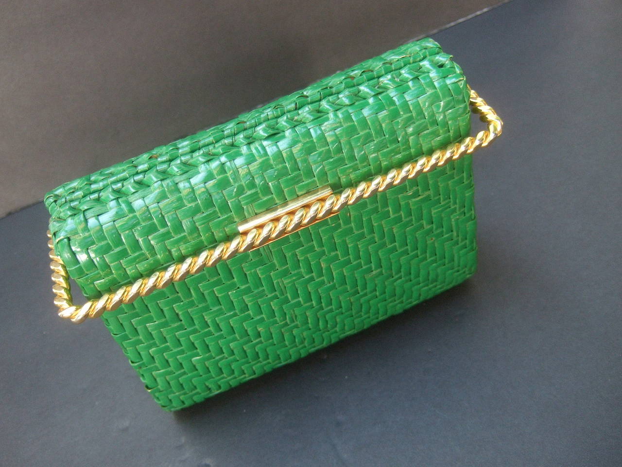 Rodo Italy Emerald green gilt trim wicker clutch bag c 1980s
The stylish Italian clutch bag is covered with woven wicker
bands on all sides. The sleek retro clutch bag is framed 
with a gilt metal bar that serves as the clasp mechanism 

The