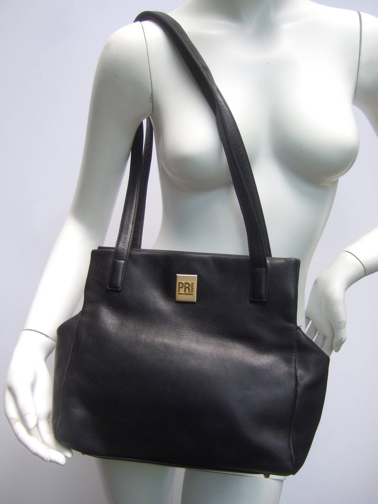 Paco Rabanne Paris Black leather shoulder bag c 1980s
The classic saddle style shoulder bag is covered in supple
black leather. Designed with twin leather shoulder straps
The front exterior is adorned with a gilt metal emblem 
stamped Paco