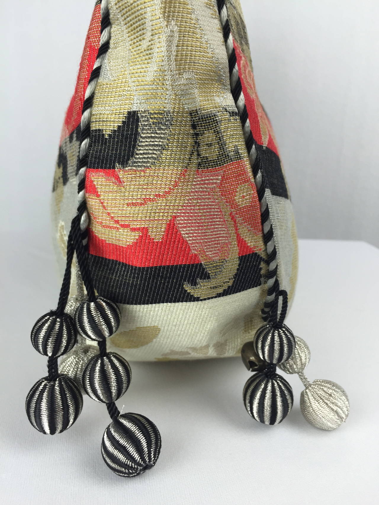 Charming Asian inspired damask cloth bucket bag by Alexander Mcqueen.  Gold leaves twining on what feels like upholstery fabric. Piped with silver and black twisted satin.  Frog closure. Adorned on each side by a set of metallic pom poms and bells