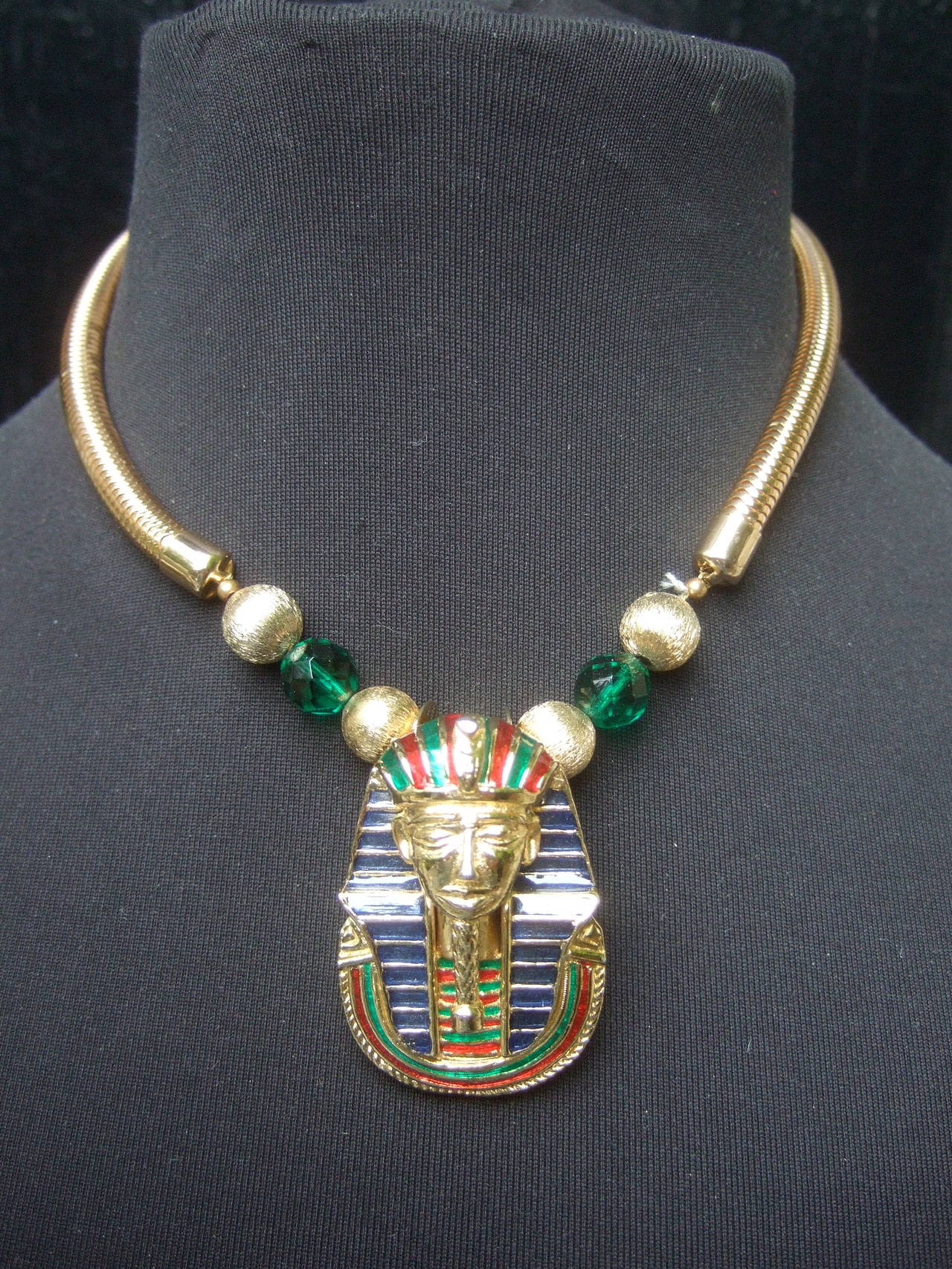 Egyptian style gilt enamel pharaoh choker necklace by Gay Boyer
The pendant necklace is adorned with a pharaoh figure accented 
with enamel detail. The pharaoh has a gilt metal snake at the center
of the headpiece 

The pendant is suspended