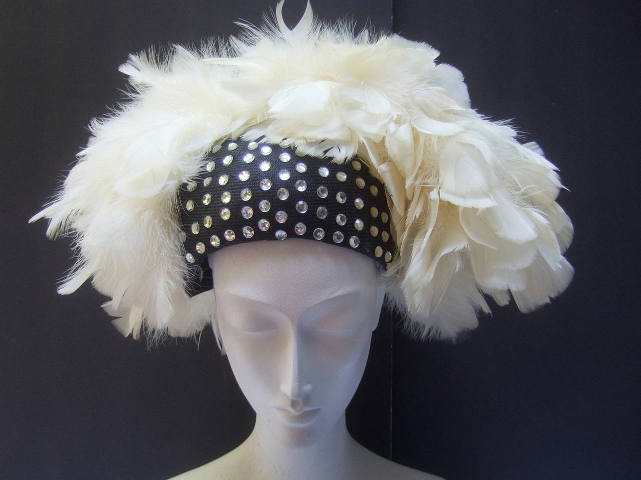 Adolofo Flamboyant jeweled feather hat c 1970
The dramatic hat is designed with diamante lucite
crystals on the center panel that illuminate against 
the black straw background 

The sides, top & back are embellished with 
exotic fluffy white