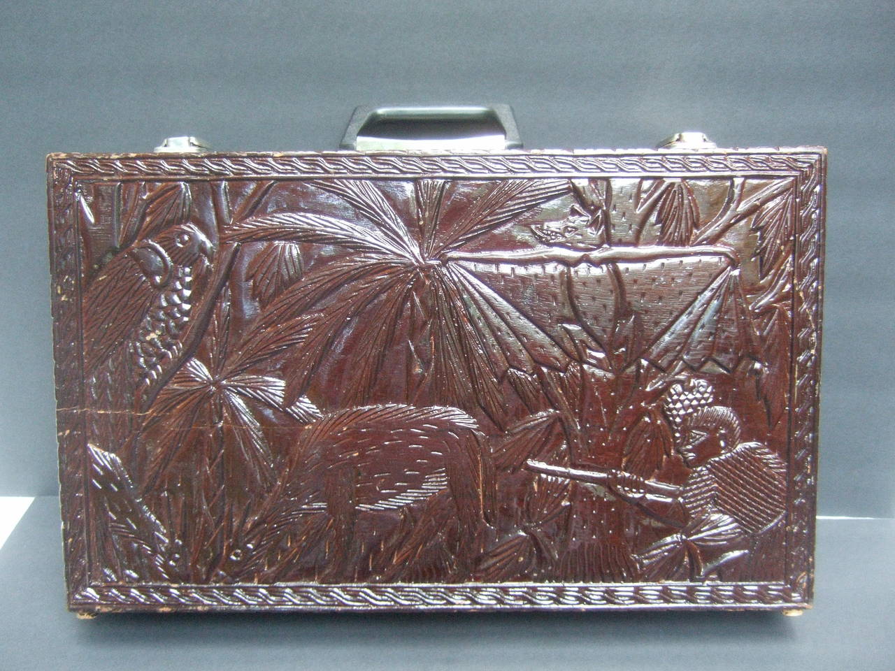 Exotic wood hand carved topical jungle brief case c 1970s
The unique rustic handmade wood brief case is illustrated 
with a lush jungle scene with a hunter in pursuit of
wild boar. The tropical jungle landscape is illustrated 
with a menagerie