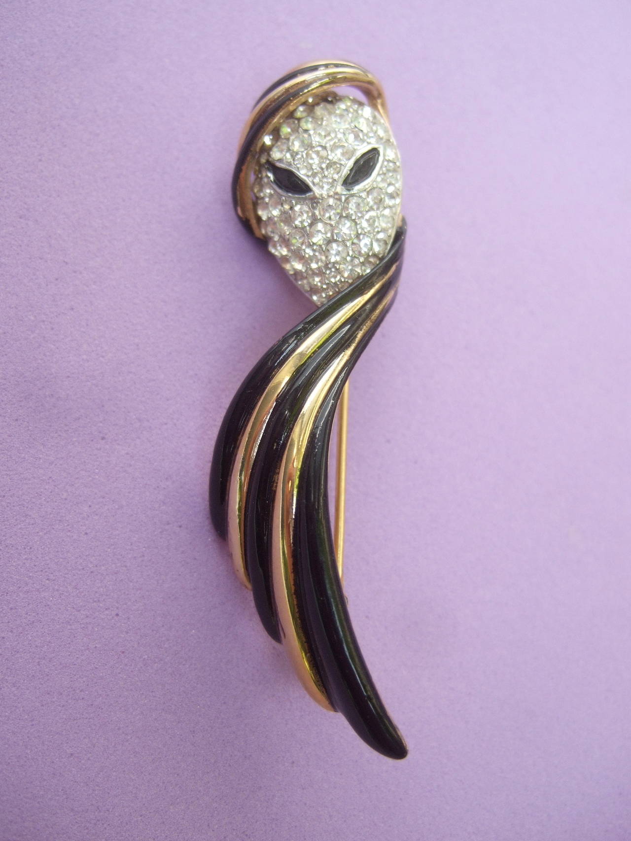 Trifari phantom of the opera figural mask brooch c 1970
The unique brooch is designed with a mysterious 
figure encrusted with glittering diamante crystals
covering the face

The stylish figure is wearing a black enamel turban 
with sleek gilt