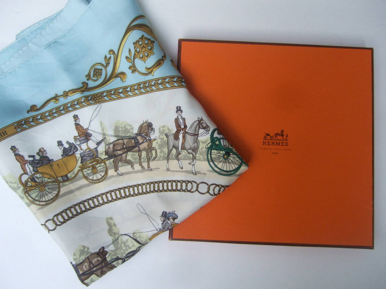 Hermes Paris La Promenade De Longchamps silk scarf in Hermes Box
The elegant designer scarf is illustrated with a wreath of horse drawn 
carriages. The center graphics capture a roamntic courting couple   

The corner edges are a luminous ice