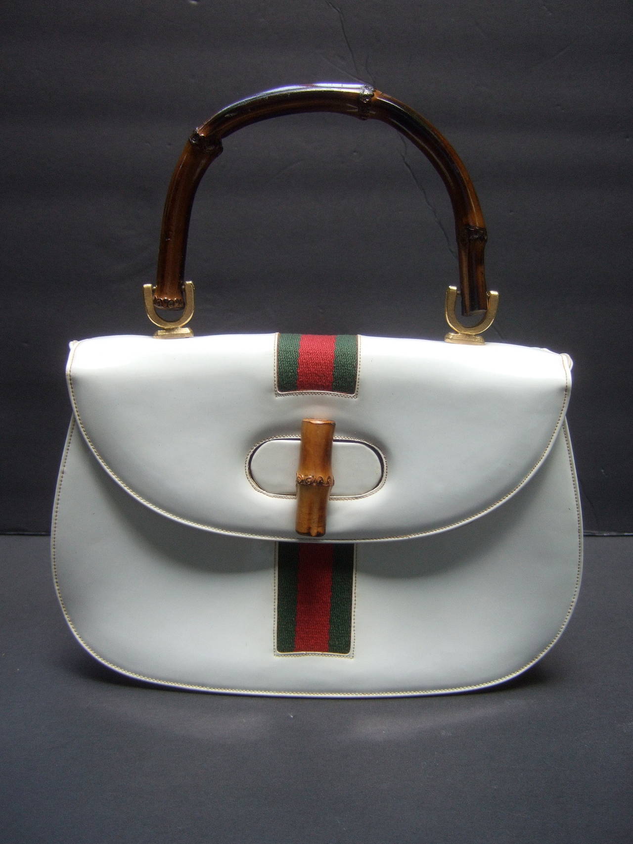 Saks Fifth Avenue White patent leather bamboo handle handbag c 1970
The stylish retro handbag is designed with a red & green canvas stripe
The posh handbag is carried with a wood bamboo handle with a wood
bamboo toggle clasp

The canvas red &