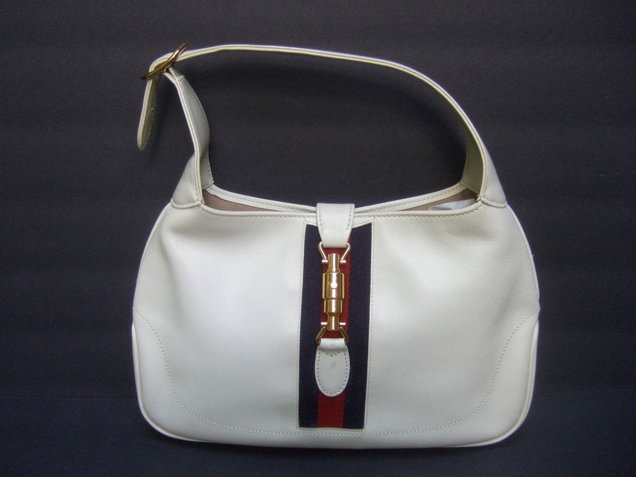 Gucci Italy Rare bone leather webbed piston handbag 
The chic Italian leather handbag is designed with a gilt
metal piston clasp mechanism. Accented with Gucci's
signature red and blue webbed stripe  

The iconic Gucci handbag design became