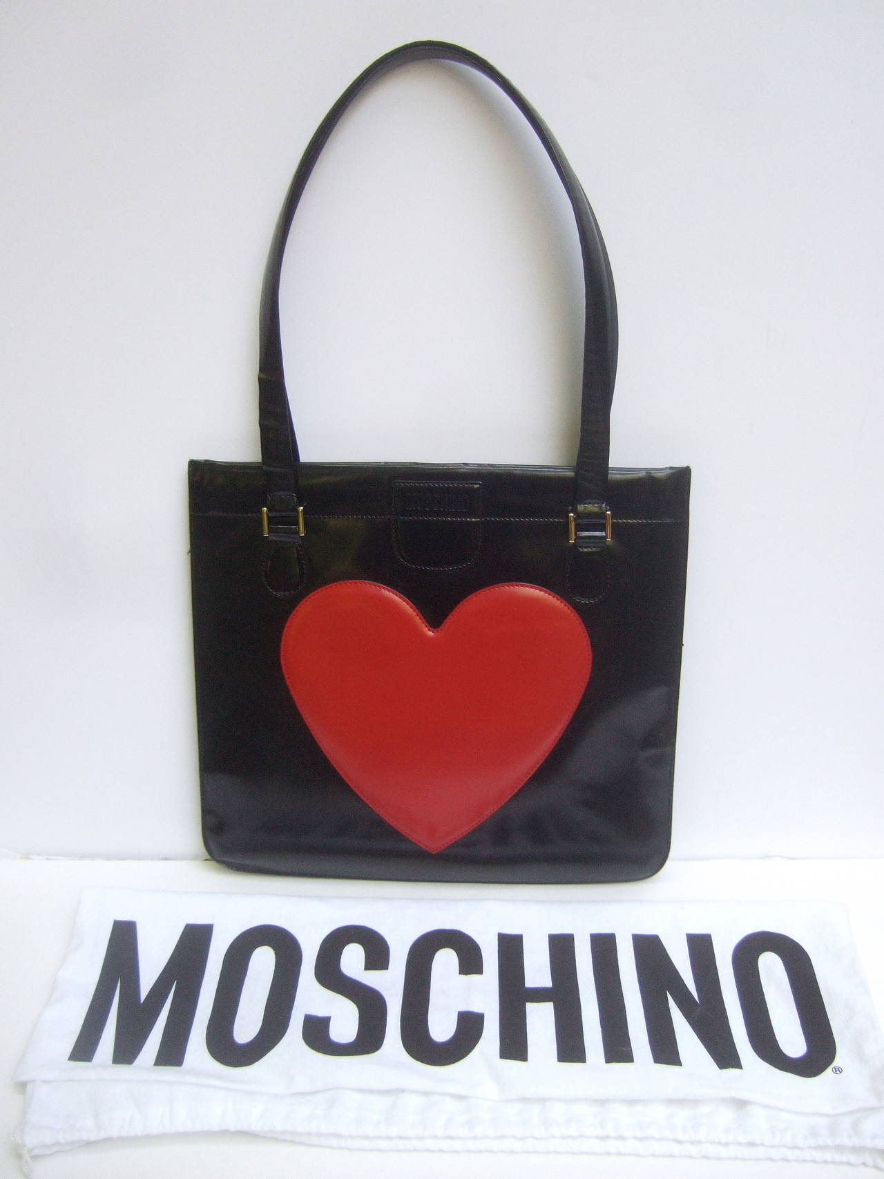 Moschino Italy Mod heart black waxed leather handbag
The stylish Italian handbag is designed with a large 
applique heart. The front exterior panel is embossed
Moschino

The chic designer tote style shoulder bag is carried with
twin black