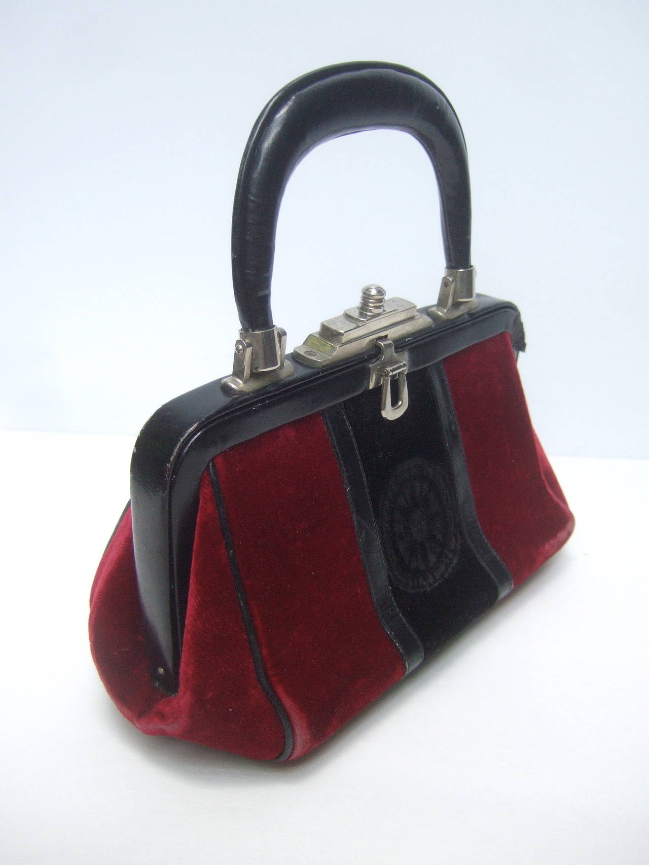 Roberta di Camerino Burgundy red & black velvet leather handbag c 1970
The chic Italian handbag is covered with dark red velvet with
a center black cut velvet panel with a radiating sun symbol

The clasp frame is black leather with chrome metal