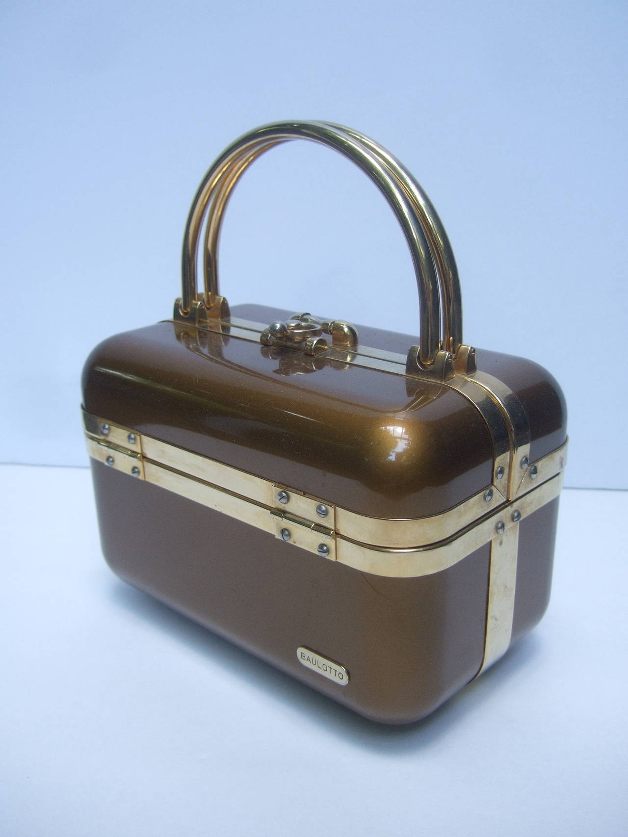 Sleek 1970s Italian bronze lucite handbag designed by Baulotto
The posh Italian handbag is designed with glossy gold metallic 
lucite. The molded panels are accented with gilt metal bands
and hardware. Baulotto in Italian means trunk  

The interior
