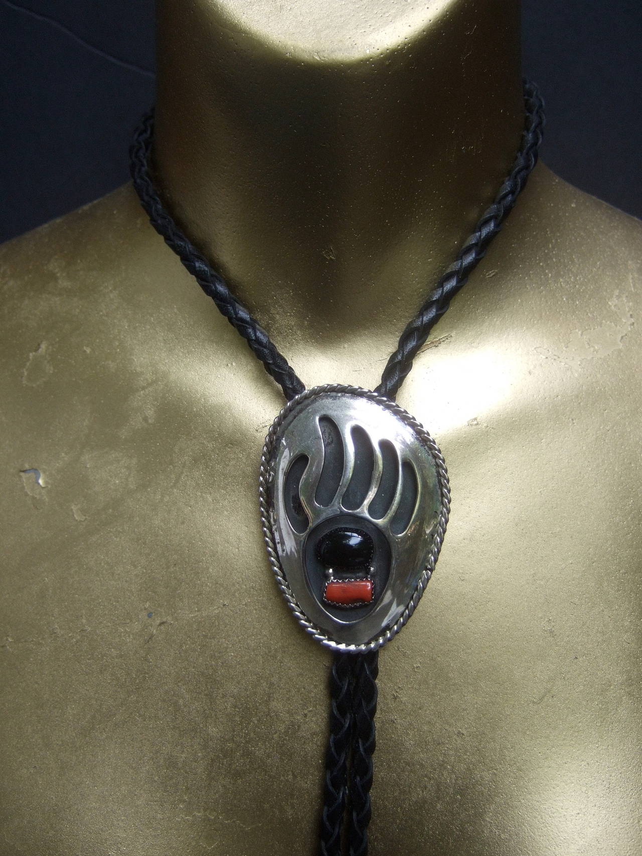 Sterling coral and jet bear claw bolo tie c 1970s
The southwestern artisan bolo tie is designed
with a sterling oval shaped pendant

The sterling bolo is designed with a coral
and oval shaped jet cabochon. The sterling
bolo pendant has cut out