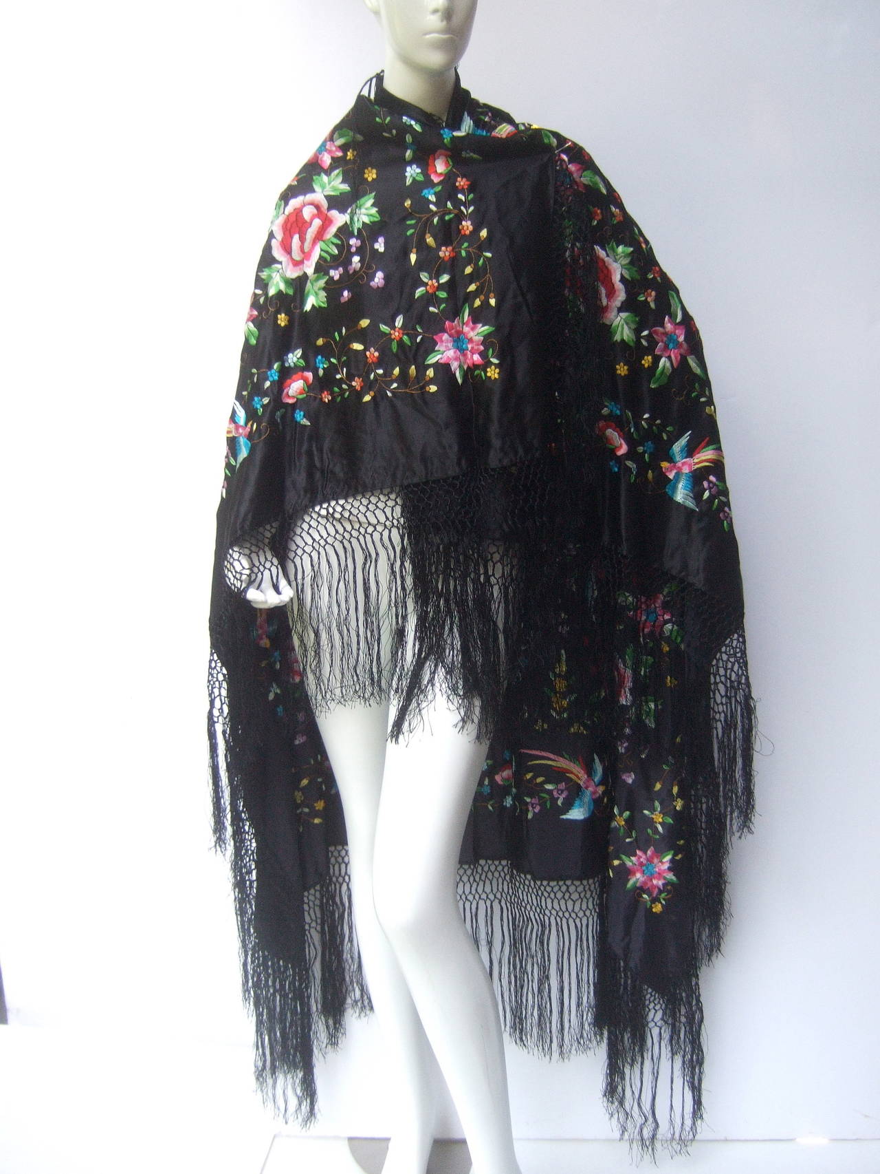 Exotic embroidered silk fringe shawl c 1970s
The opulent black silk shawl is embellished 
with elaborate hand embroidery; illustrated 
with a garden of lush flowers with soaring 
birds gliding throughout of the maze of flower 
blooms

The