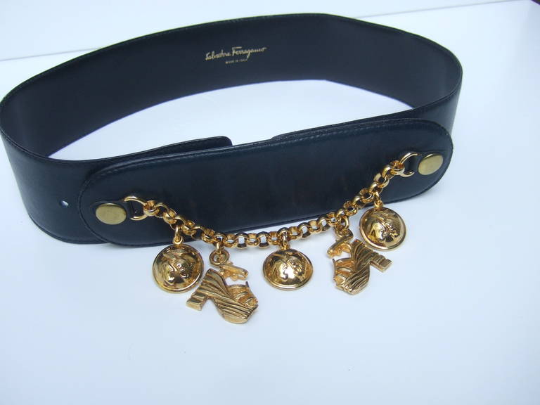 SALVATORE FERRAGAMO Stylish gilt charm blue leather belt c 1980s
The elegant Italian dark blue leather belt is embellished with five
gilt metal dangling charms. A pair of platform shoes & three circular 
dangling disc with shoe designs impressed