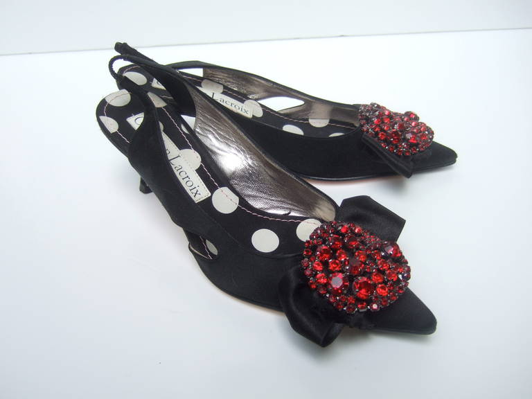 CHRISTIAN LACROIX Ruby crystal black satin slingbacks Size 36
The opulent shoes are embellished with a cluster of glittering
crystals placed on a black satin bow. The sides have a unique 
peak a boo slit. The shoes are lined with festive polka