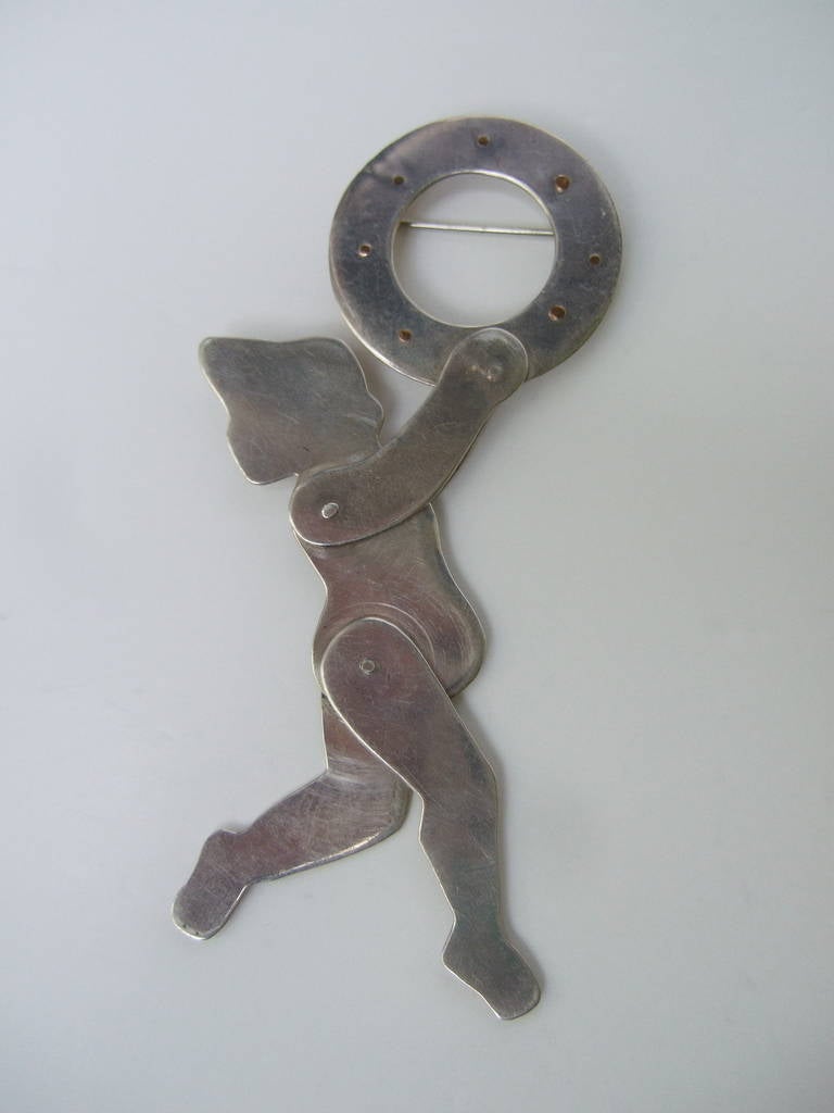 Spilla artigianale figurata articolata in argento di Ann Biederman, 1990 ca.
Questa spilla unica, fatta a mano, è disegnata con un bambino in varie forme.
posture che suonano. Il braccio articolato, le gambe e il cerchio si regolano e cambiano