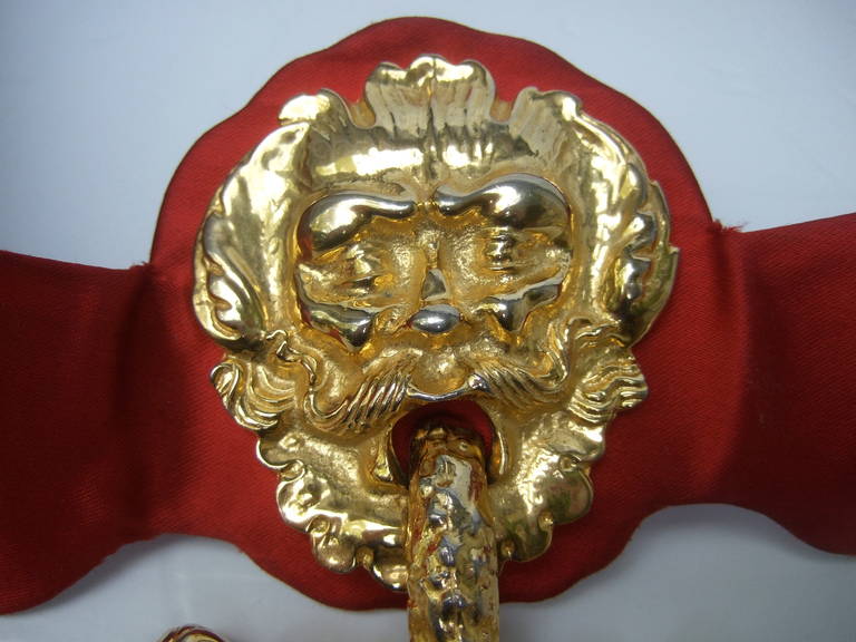 JUDITH LEIBER Massive figural gilt metal door knocker ruby satin belt c 1980

The extraordinary belt is adorned with an incredible gilt metal hinged
buckle. The huge ornate buckle is designed with a mythical figure at the center

The dangling