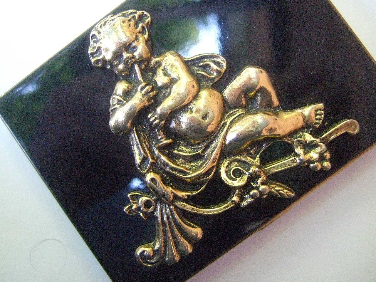 Ornate gilt pan figure black enamel cigarette case c 1950
The unique cigarette case is decorated with the figure of Pan playing his flute 
The stylish cigarette is covered with black enamel. The interior is gilt metal designed with a spring clasp