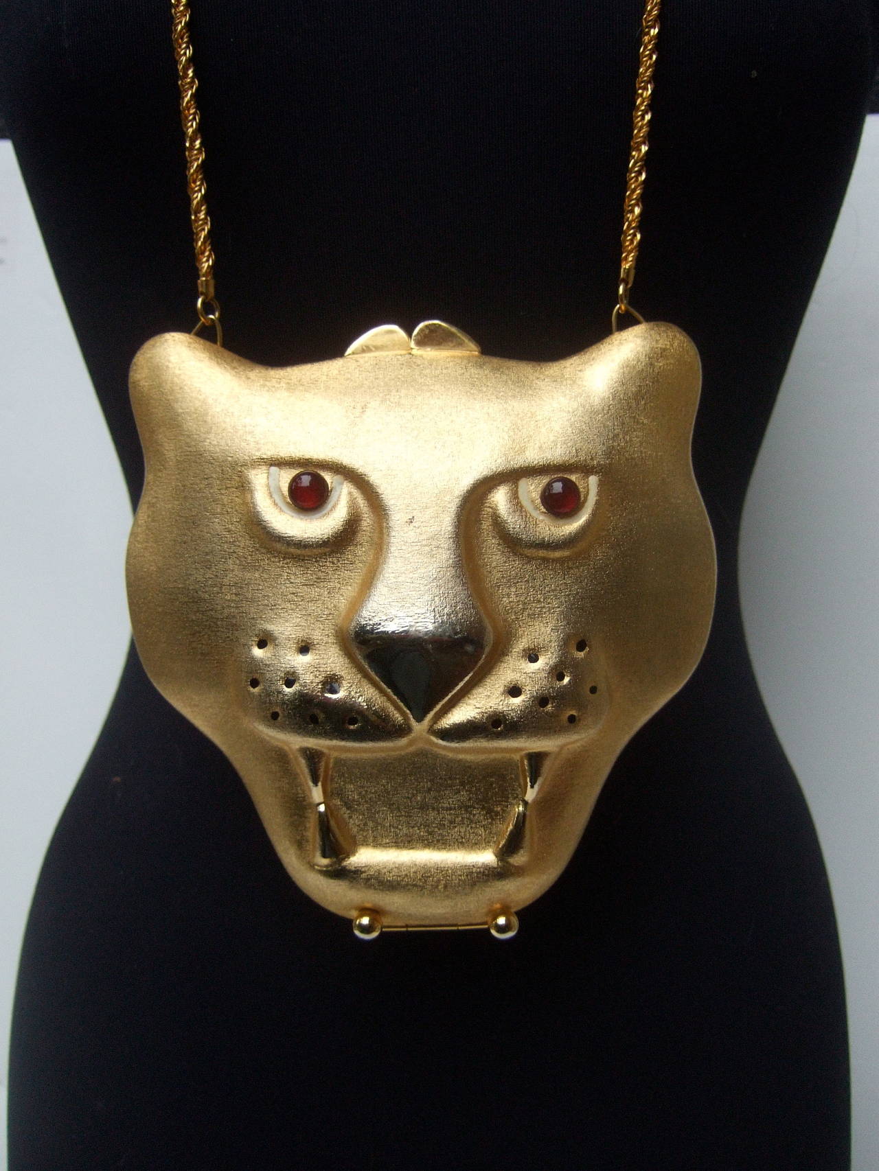 SAKS FIFTH AVENUE Gilt metal evening bag Made in Italy c 1970
The opulent minaudiere purse is designed with an exotic gold metal panther's head
The eyes are embellished with ruby color glass cabochons accented
with black enamel impressed