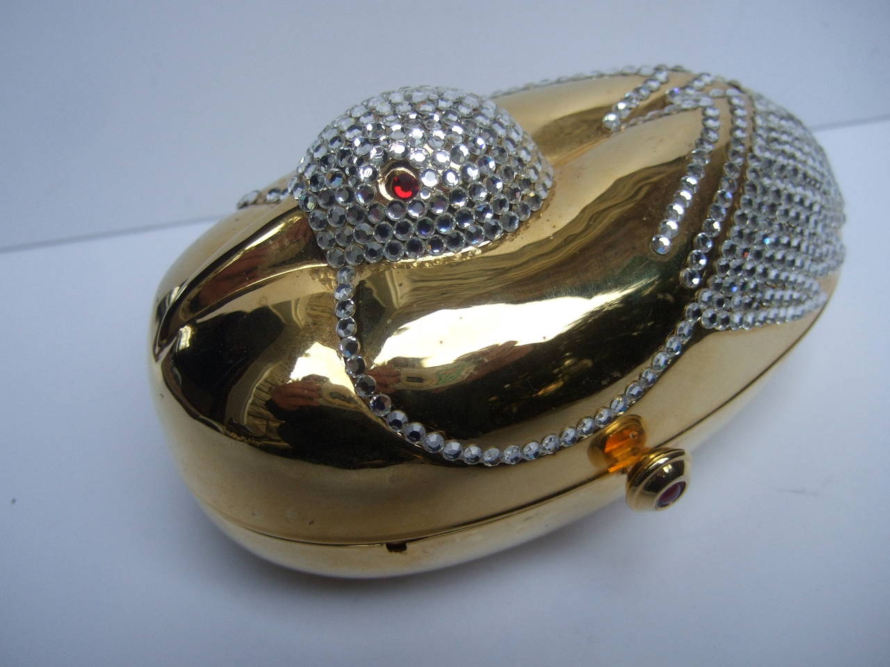 Opulent jeweled gilt metal bird evening bag c 1980
The elegant figural minaudiere evening bag is designed with a nesting bird encrusted with glittering diamante crystals. The brilliant crystals illuminate against the sleek gilt metal. The bird's
