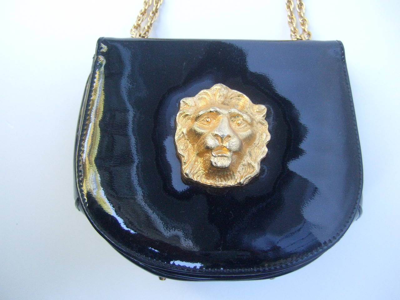 Saks Fifth Avenue Black patent leather diminutive handbag c 1970
The stylish retro handbag is adorned with a gilt metal lion emblem
The compact patent leather handbag is carried with dual gilt metal
chain straps

The interior is lined in black