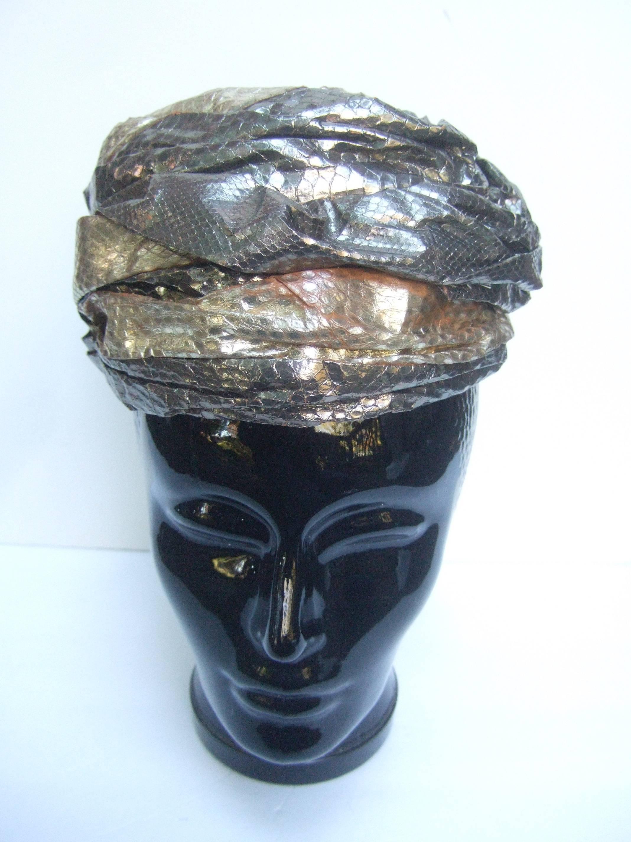 Avant-garde Metallic snakeskin turban c 1960
The unique turban is designed with bands
of exotic metallic snakeskin 

The snakeskin bands range from gold
to pewter tone metallic dyed snakeskin
The snakeskin bands are wrapped 
around the turban