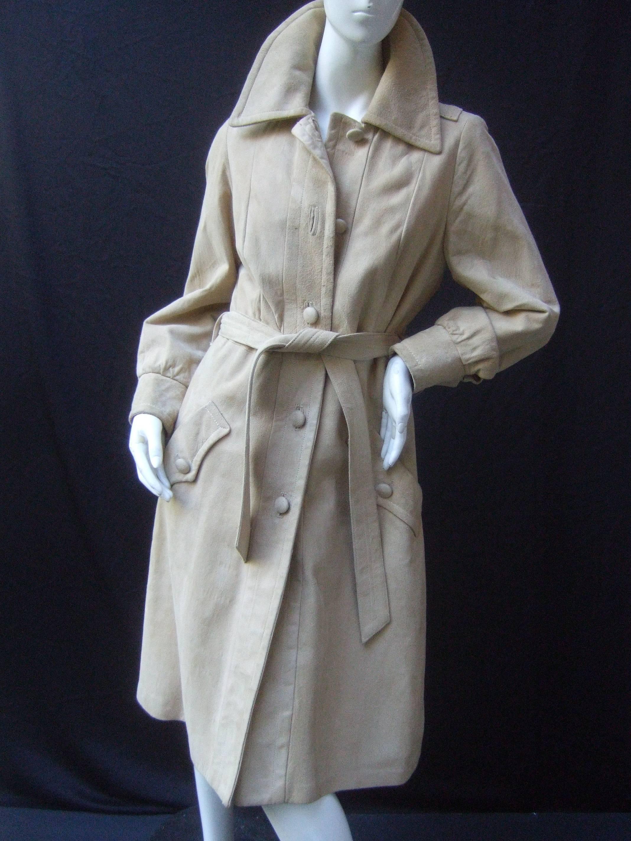 1970s Plush tan doeskin suede belted trench coat
The stylish coat is designed with powdery soft suede
The collar has wide lapels that can be folded up around 
the neck

The coat secures with five suede covered matching
buttons that run down