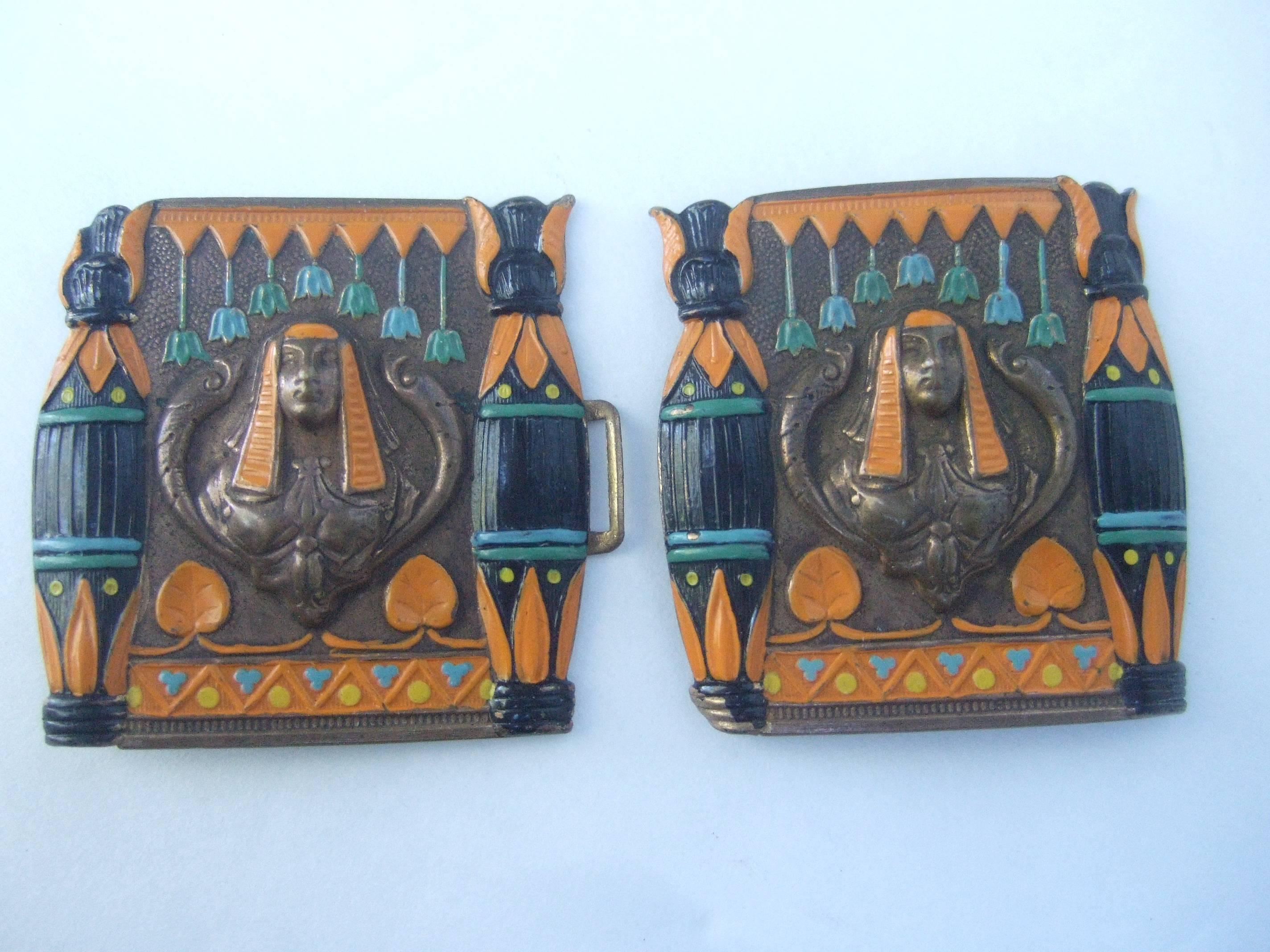 Egyptian revival enamel Pharaoh belt buckles
The unique pair of metal buckles are designed 
with repousse Pharaoh figures at the center;
surrounded by coiled snakes on each side
of their heads

The burnished copper metal buckles are
accented