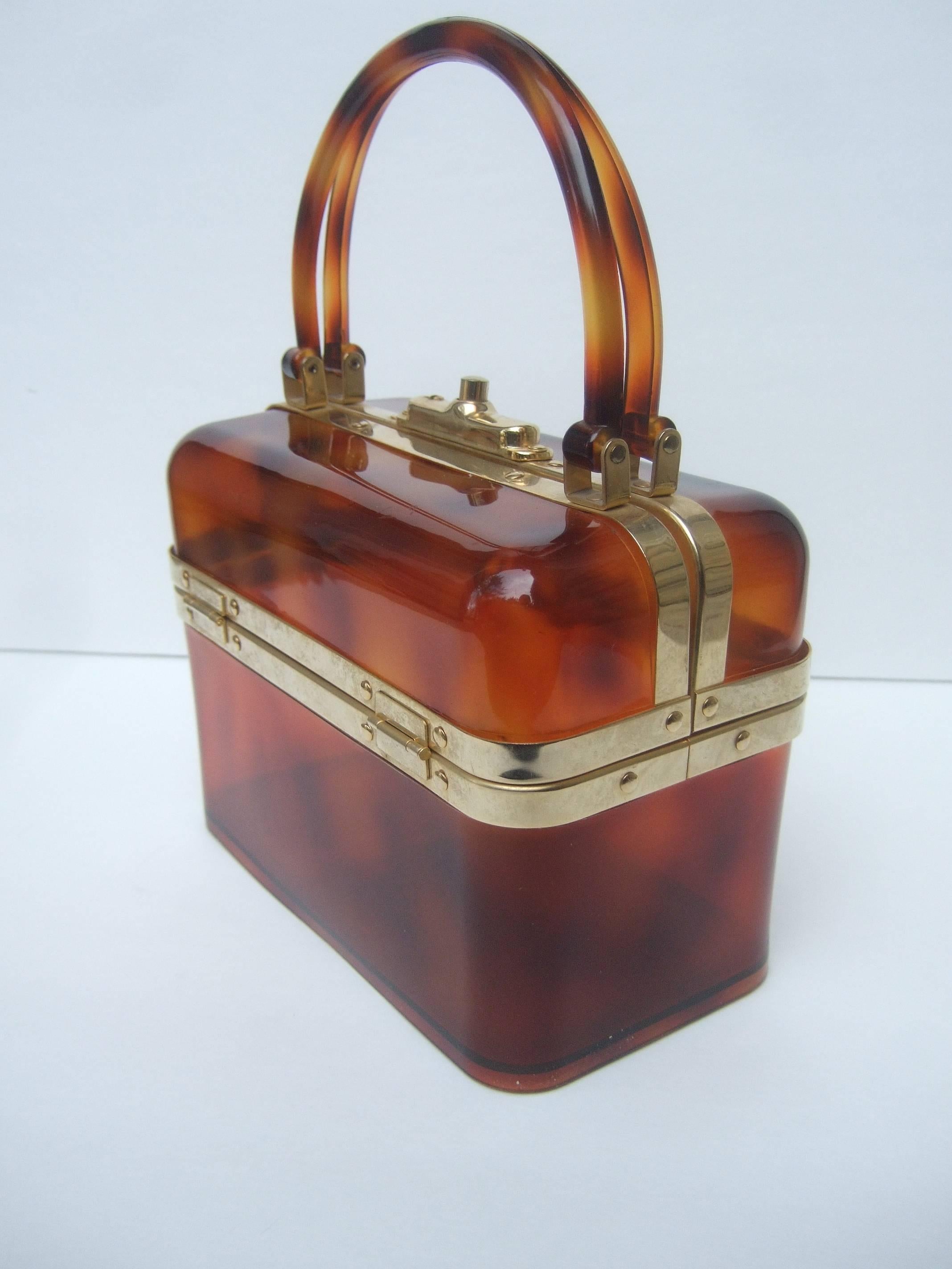 Sleek tortoise shell lucite handbag Made in France c 1970
The stylish retro box shaped handbag is designed
with translucent brown lucite with gilt metal trim
and hardware 

The chic handbag is carried with twin matching 
lucite swivel handles.
