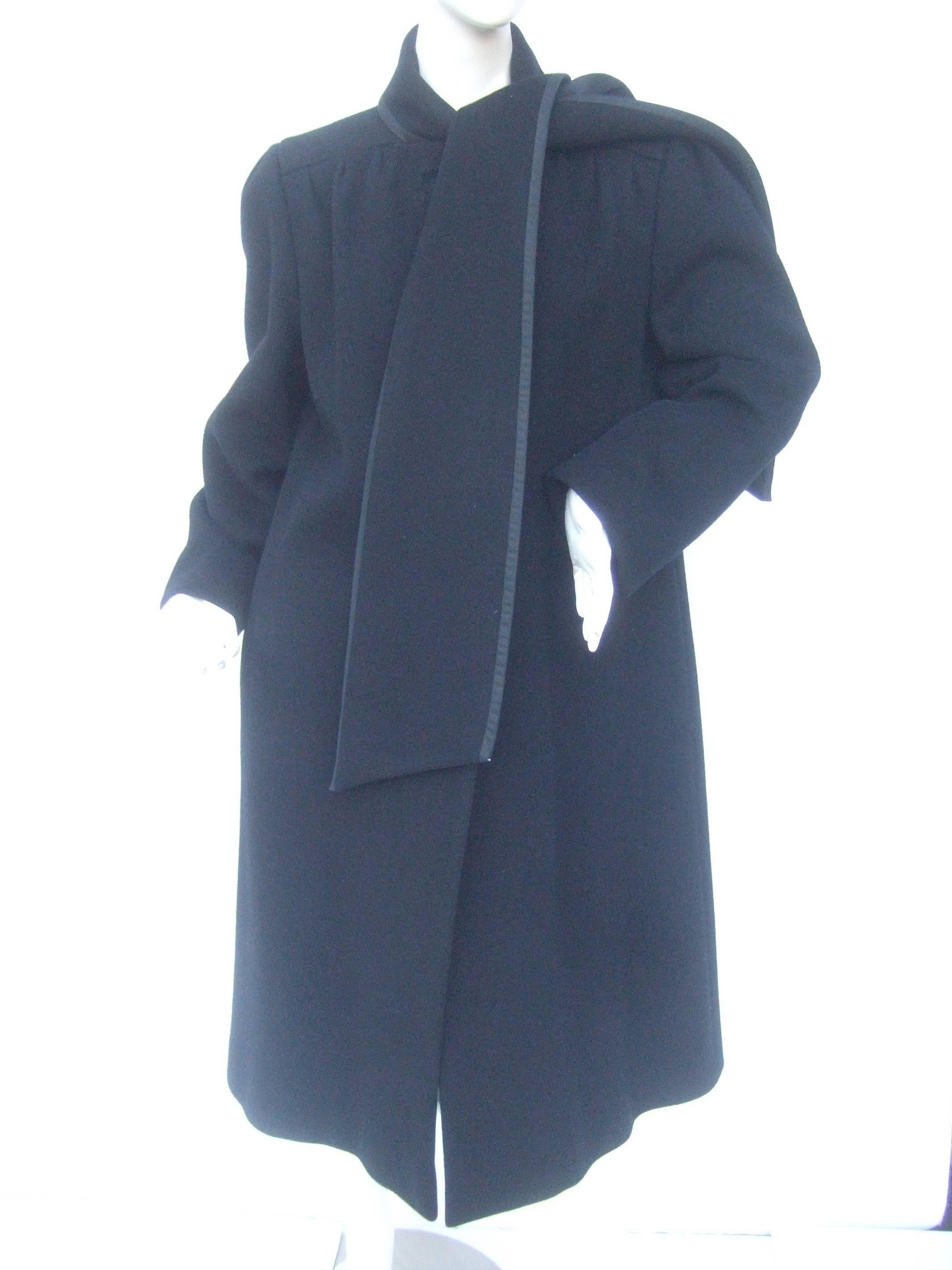 Pauline Trigere Unique black wool winter coat with built in scarf
The stylish coat is designed with a wide dramatic built in collar 
scarf that can be draped over the shoulders or left loose running 
down the the front

The scarf is trimmed