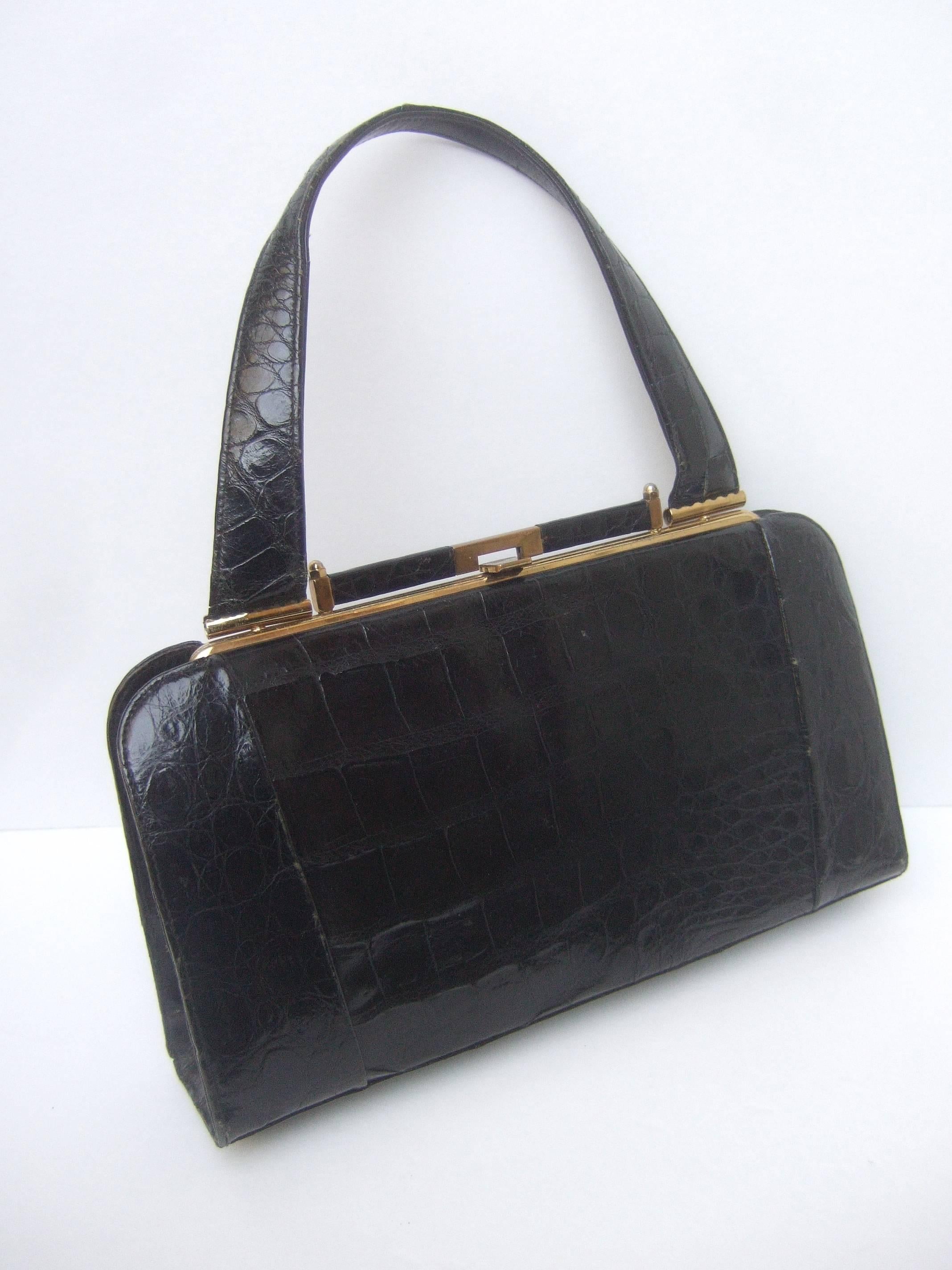Sleek ebony vintage alligator leather handbag ca 1960s
The stylish retro handbag is covered with glossy black 
alligator skin

The handbag is designed with a sleek
gilt metal clasp frame and hardware
The interior is lined in ivory color