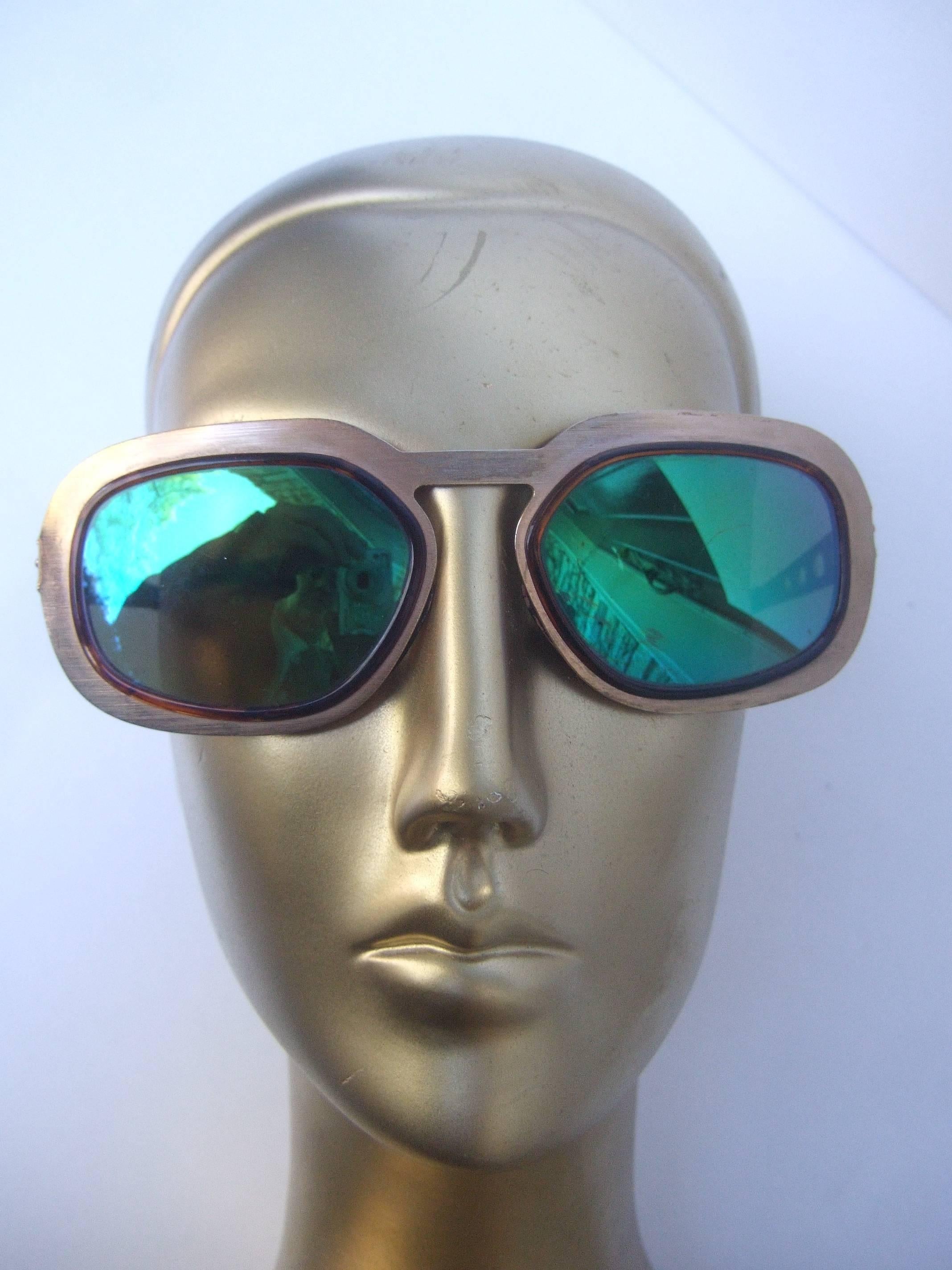 Sleek gilt metal green tinted sunglasses Made in Italy 1970s 
The mod retro sunglasses are designed with brushed
gilt metal frames. The plastic lenses have a green 
reflective tinted coating 

The sides of the frames are accented with oval