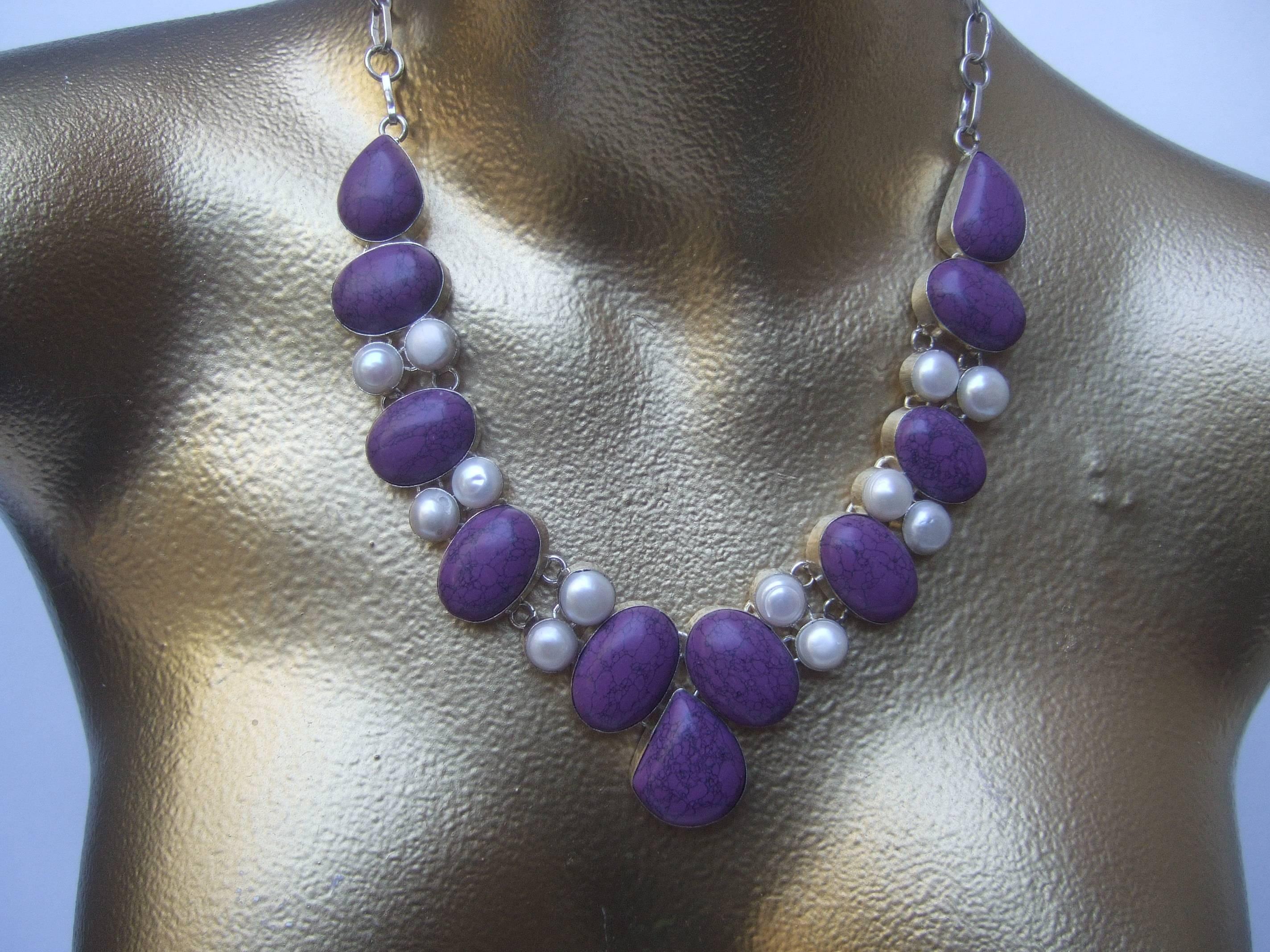 Sterling artisan purple stone and pearl statement necklace
The exotic necklace is designed with a collection of smooth
deep purple oval shaped stones set in sterling bezels

Interspersed within the purple stones are a series of smaller
circular