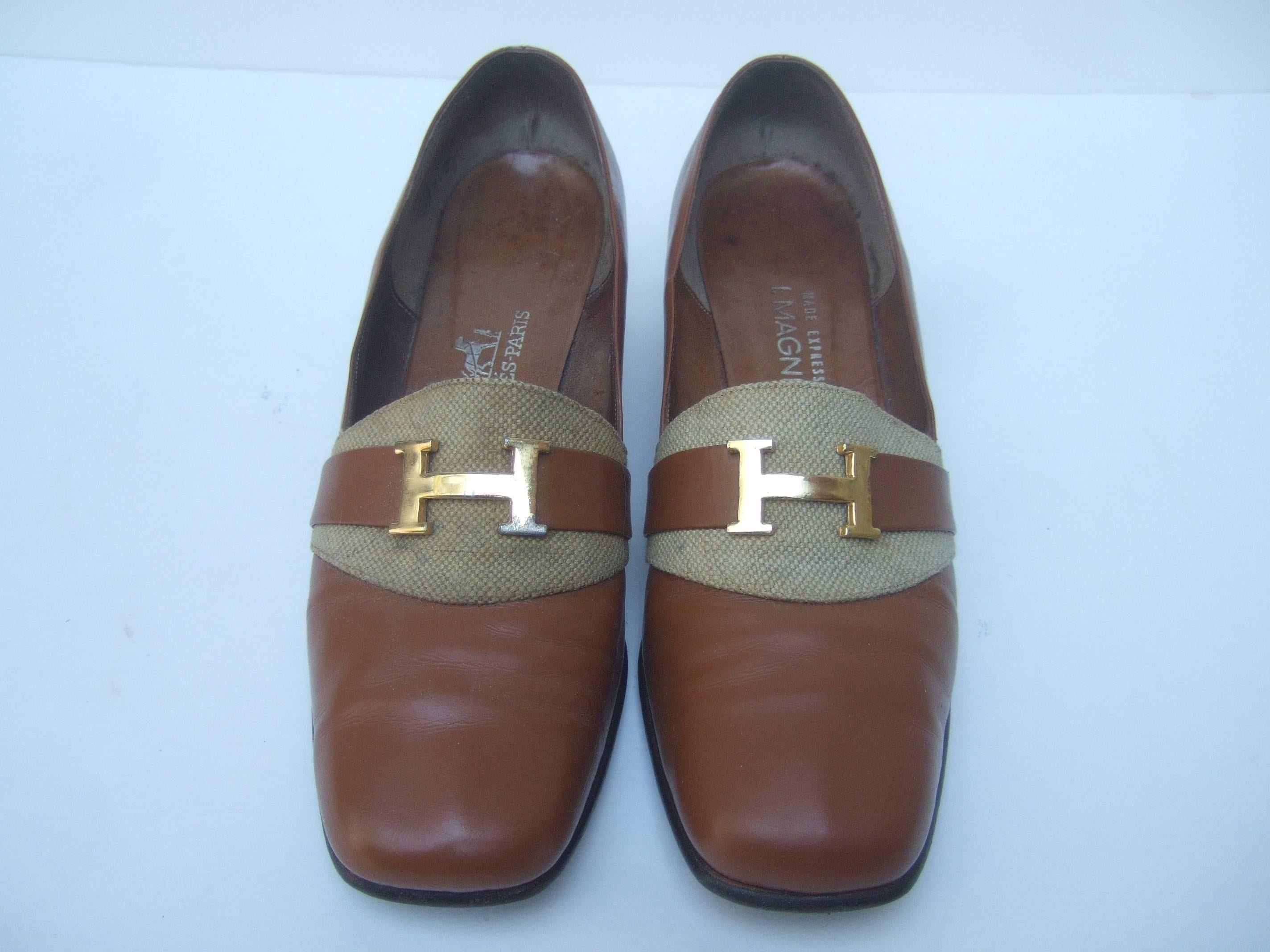 Hermes Paris Gilt H metal buckle brown leather pumps  c 1970
The classic designer pumps are covered with caramel 
brown leather. Underneath the H initials is a tan burlap
cloth panel 

The stylish retro pumps make a chic timeless