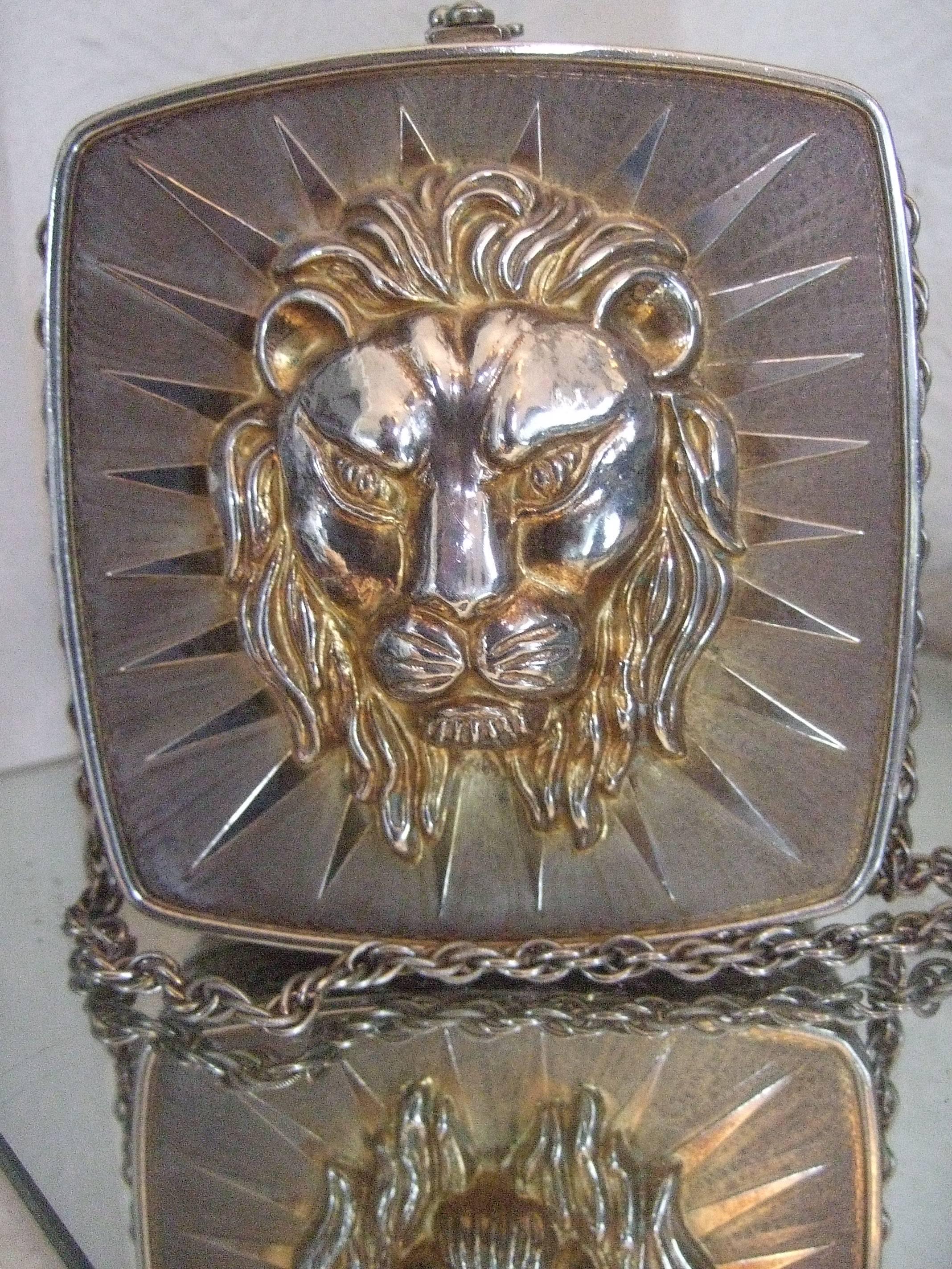 Ornate metal lion emblem evening bag Made in Italy 
The metal evening bag is decorated with a large
scale lion head replicated on both exterior sides

Etched on both exterior panels are radiating 
triangular beams that frame both lion
