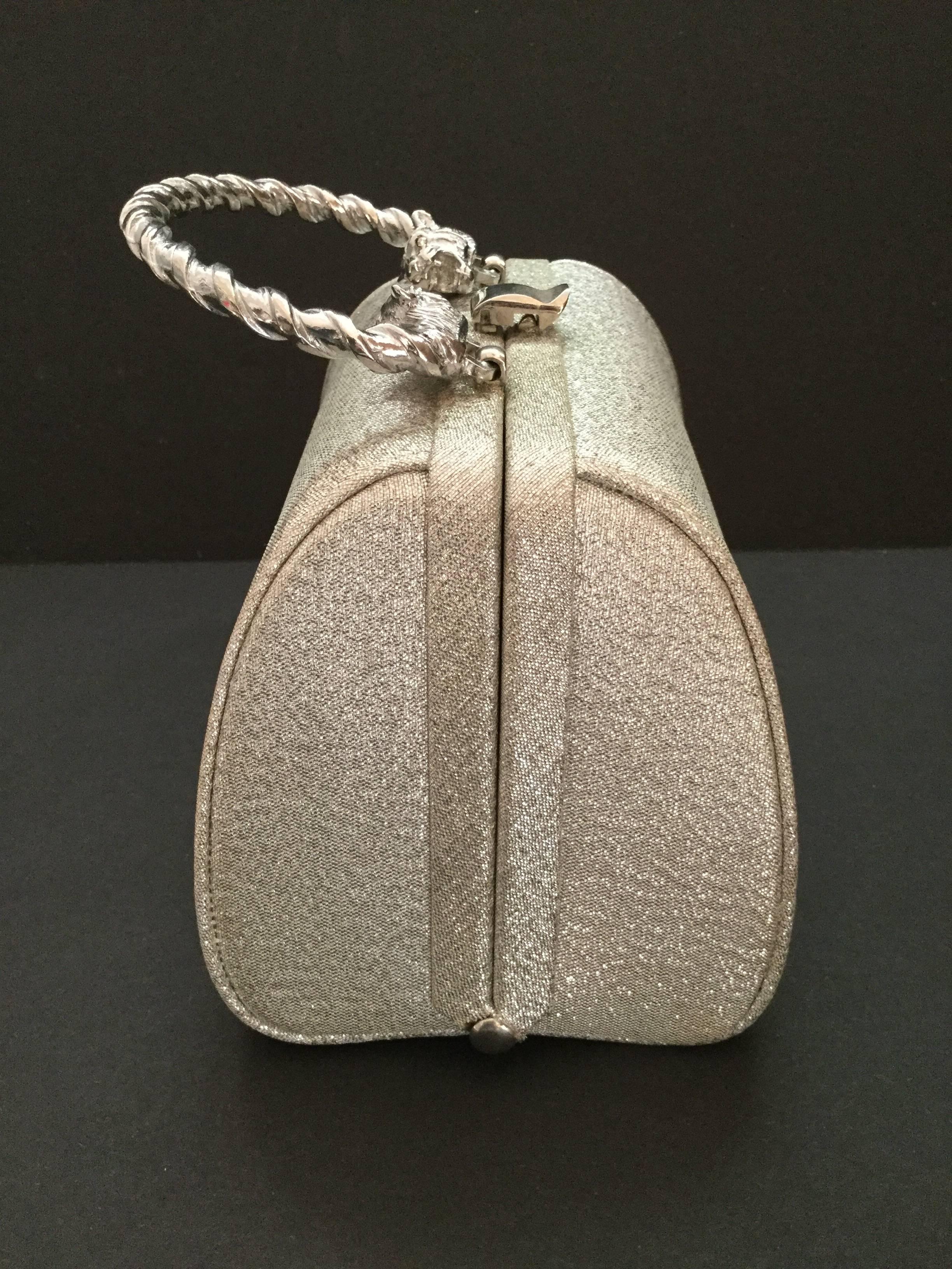 Delightful Morris Moskowitz silver lame cloth miniature evening bag with lion headed silver toned metal handle.  The lion's eyes are enlivened with clear paste crystals. Lined in pale blue satin complete with original logo mirror. 
Excellent unworn