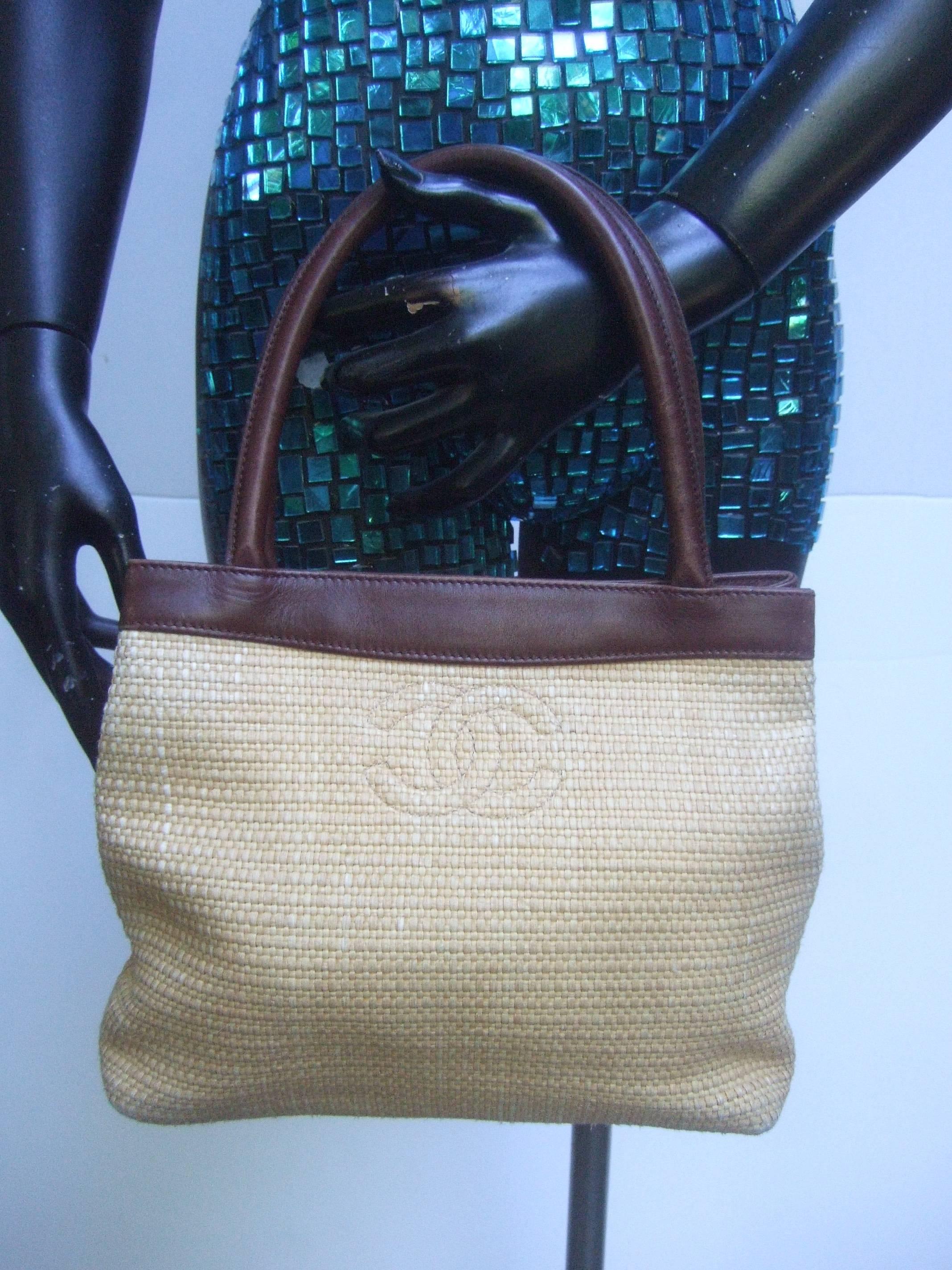 Chanel woven raffia brown leather trim handbag 
The stylish summer handbag is covered 
with natural woven raffia covering 

The front exterior panel is adorned with Chanel's
interlocked stitched C.C. initials

The small tote style handbag is