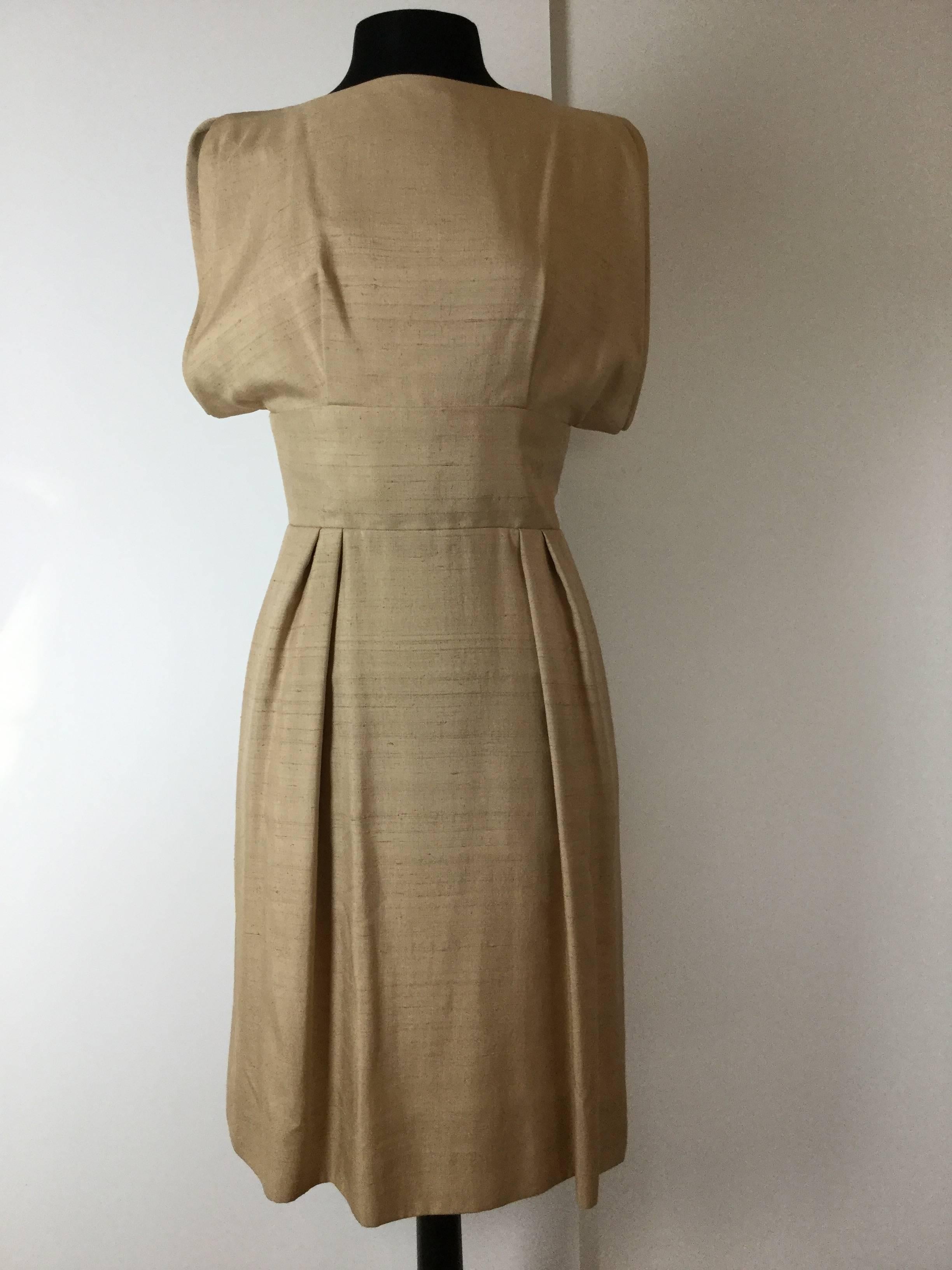 Chic raw silk beige dress probably designed by Geoffrey Beene in the early in 1960's for Teal Traina. Cool architectural cut. So simple and elegant. Fastens down the back with large black buttons.  Hidden slash pockets on both sides. 
Fully lined