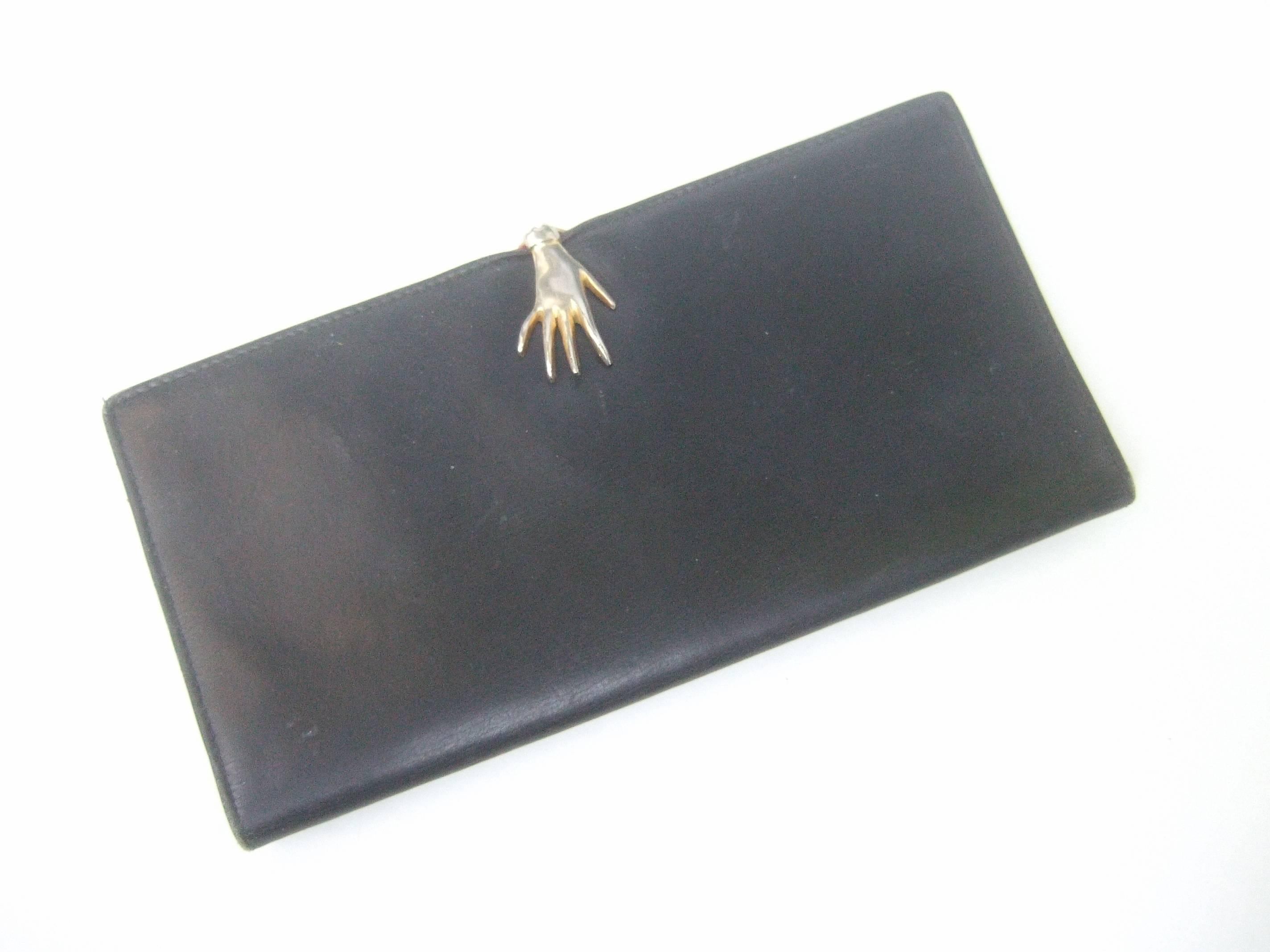 Gucci Rare black leather hand clasp wallet c 1970s
The stylish wallet is adorned with a gilt metal 
hand that serves as the clasp mechanism 

The back exterior is designed with a snap
compartment. The interior is lined in red leather
designed