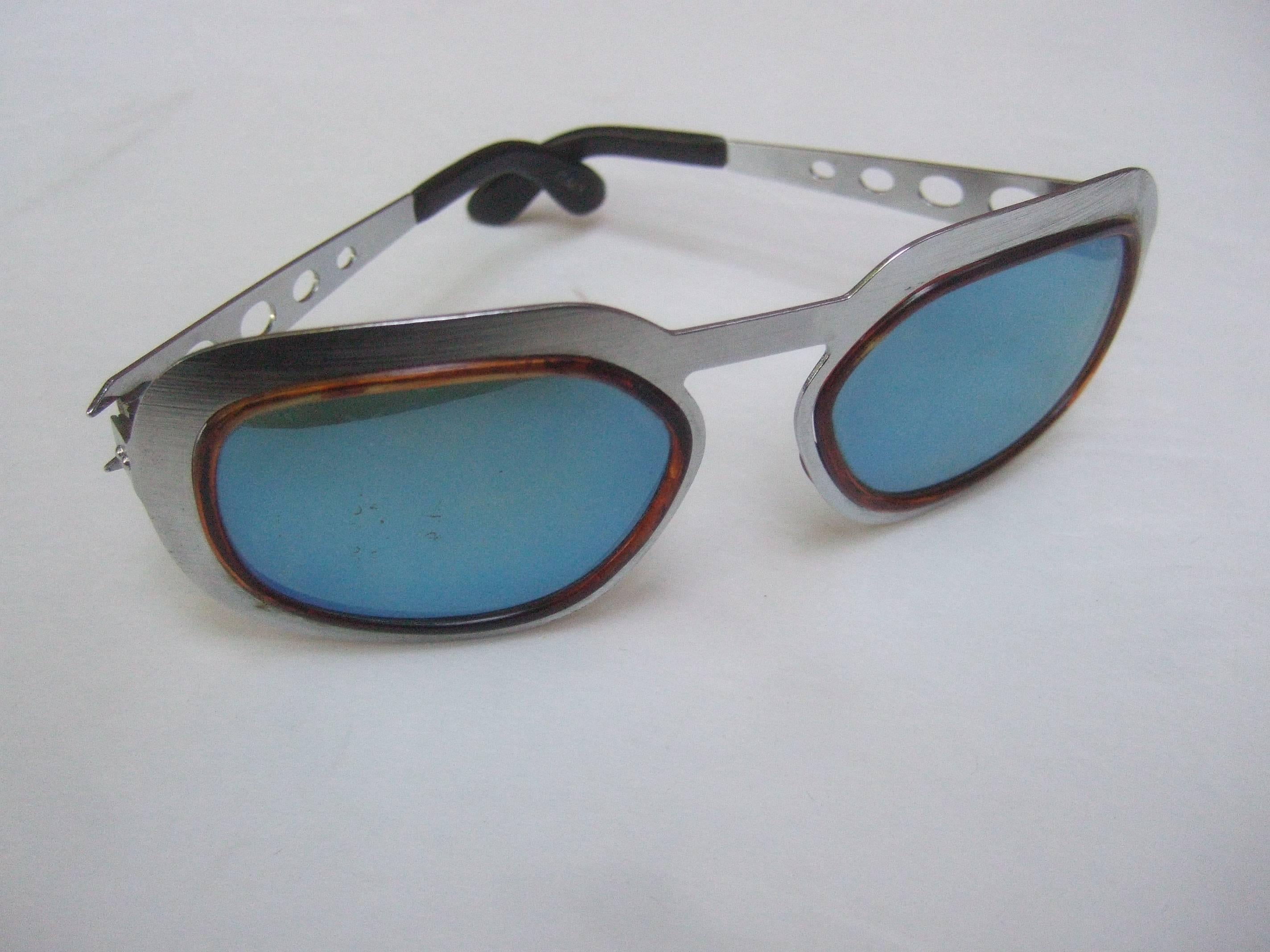 Mod Italian silver metal frame blue lens unisex sunglasses c 1970
The sleek Italian unisex sunglasses are designed with blue
tinted plastic lenses with a reflective mirrored coating

The tinted blue lenses are framed with subtle tortoise