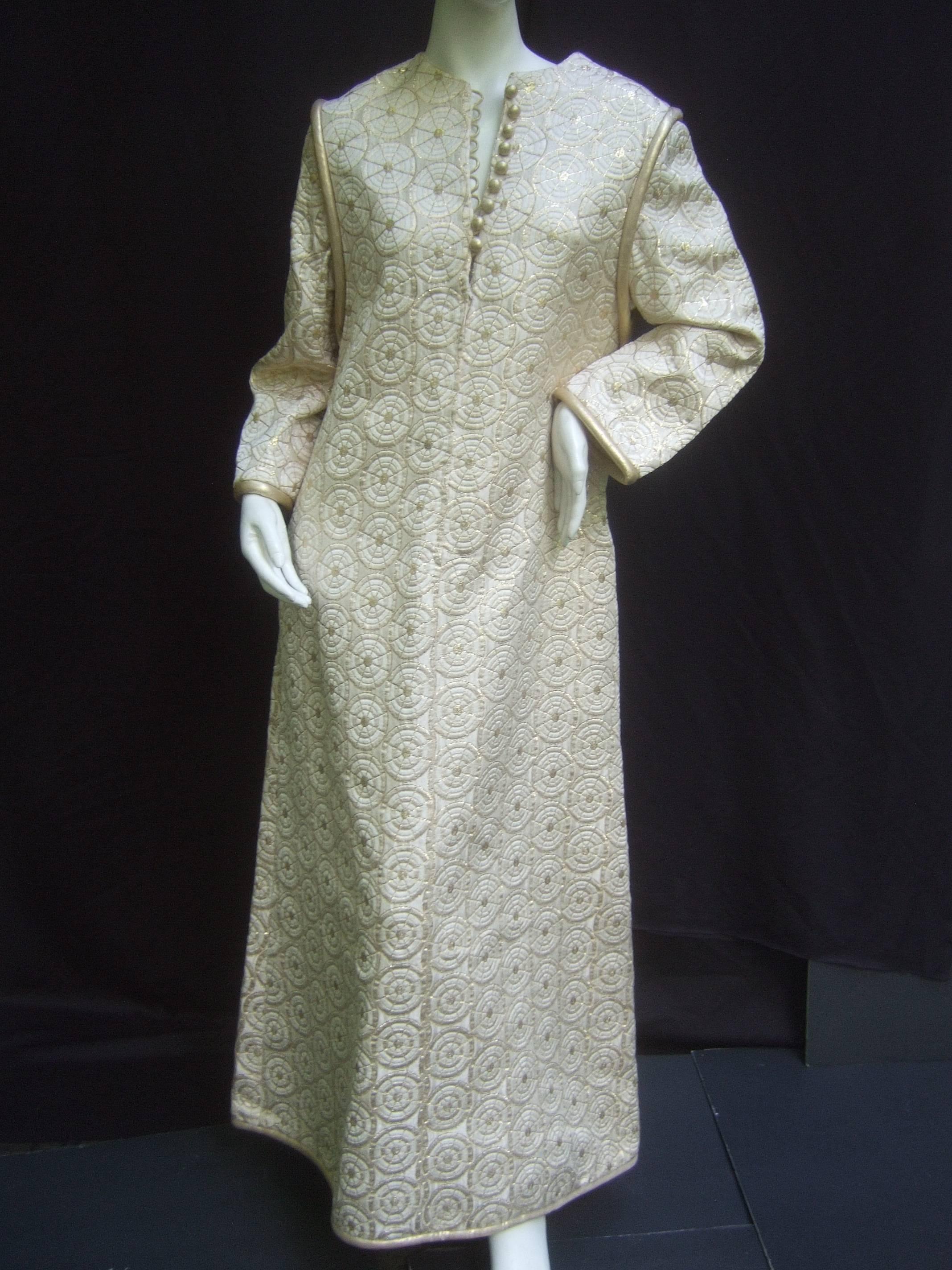 Incredibly elegant Malcolm Starr caftan of heavy brocaded creme fabric
enlivened with bullseye quilted patterns of golden metallic thread.
Two seamed pockets on either side and fully lined in a soft silky fabric.
Space age style piping at the