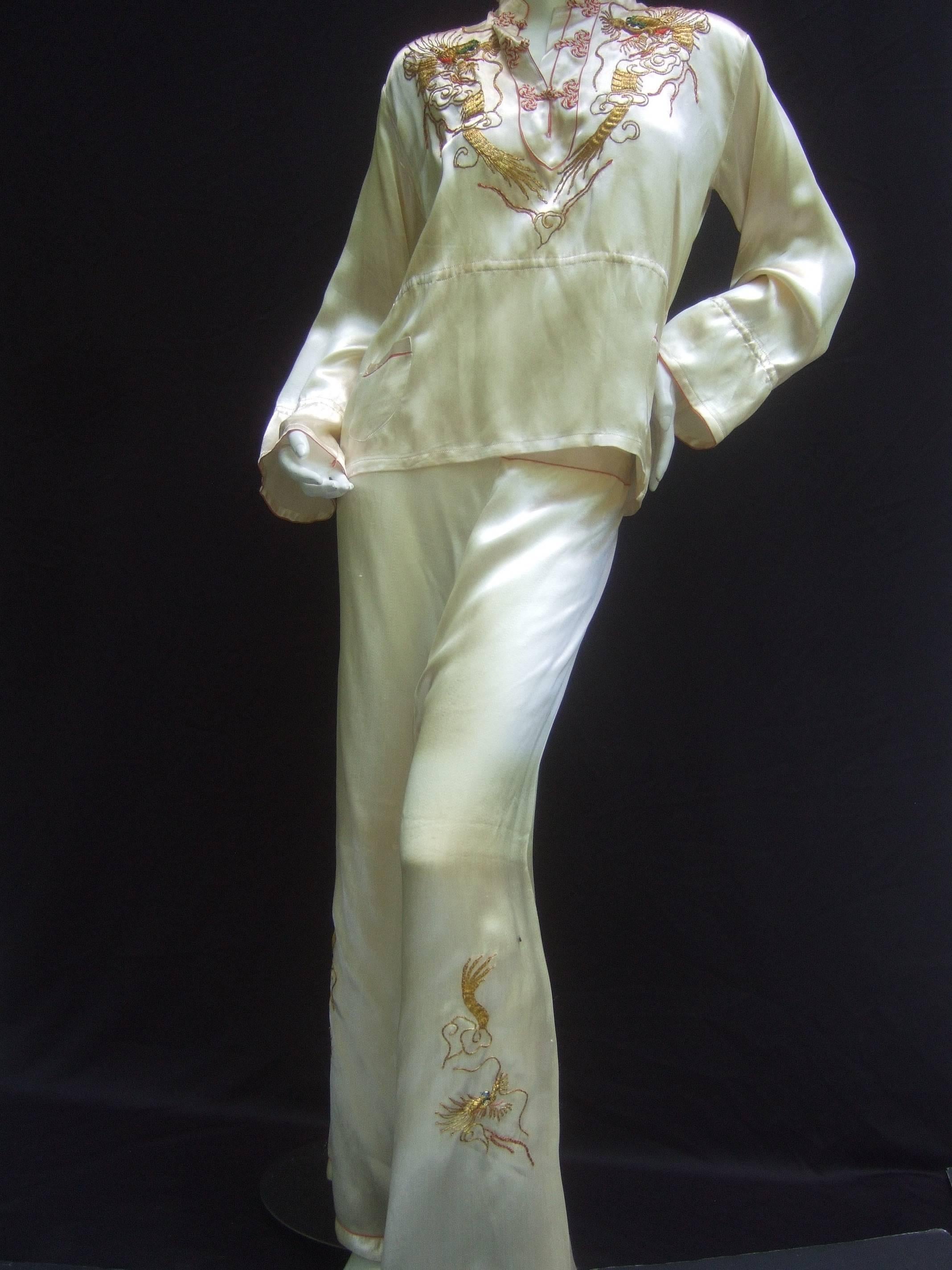 Luxurious ivory satin Asian embroidered lounge pajamas c 1950s
The exotic retro pajamas are designed with sumptuous  
satin. The tunic style blouse is embellished with exotic
gold metallic embroidery depicting dragons on the bodice
Accented with